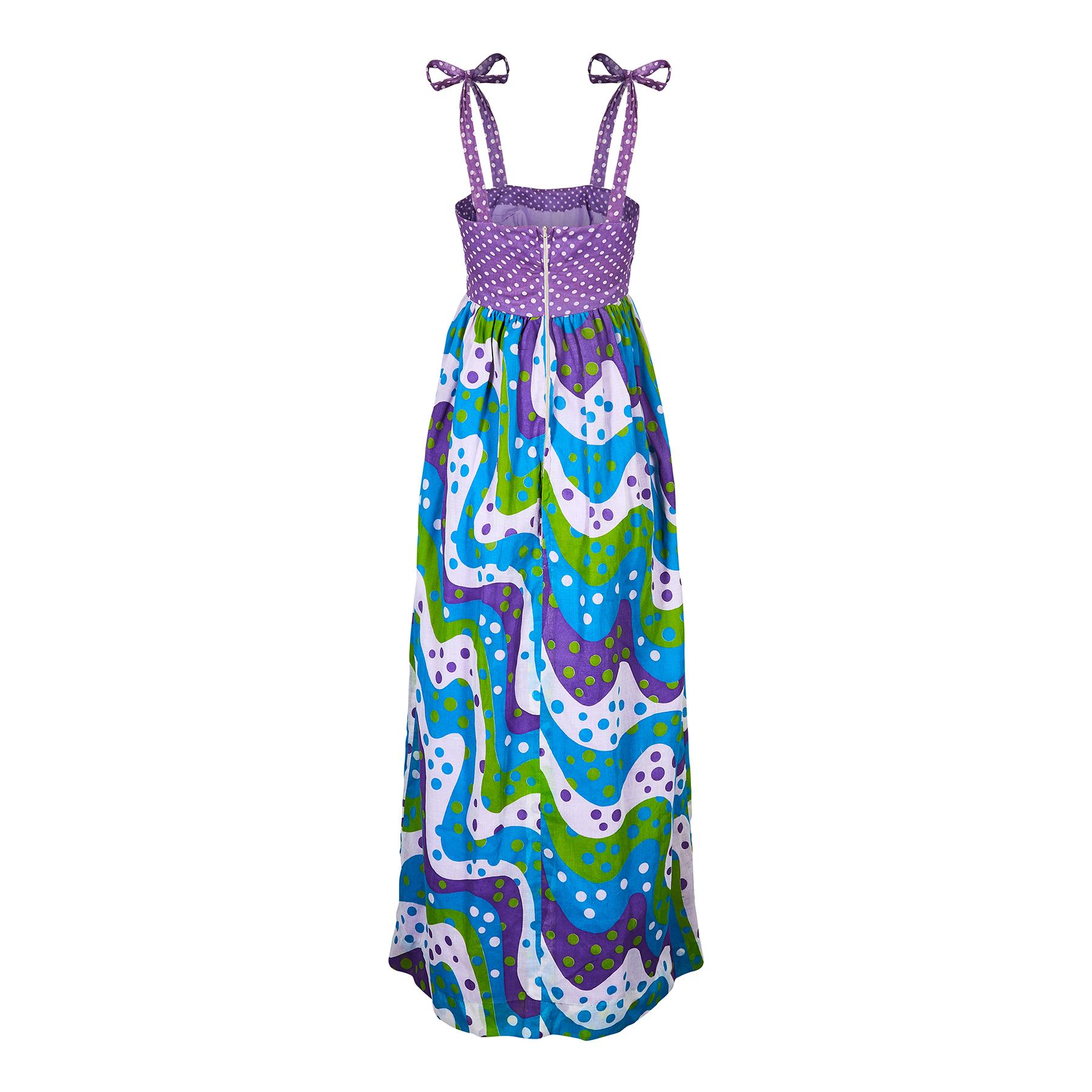 Cette robe maxi cool et originale des années 1970 combine deux types de tissus à pois dans un format audacieux. La palette de couleurs est composée de vert gazon, de sarcelle, de violet et de blanc. Le tissu est une mousseline de coton légère et