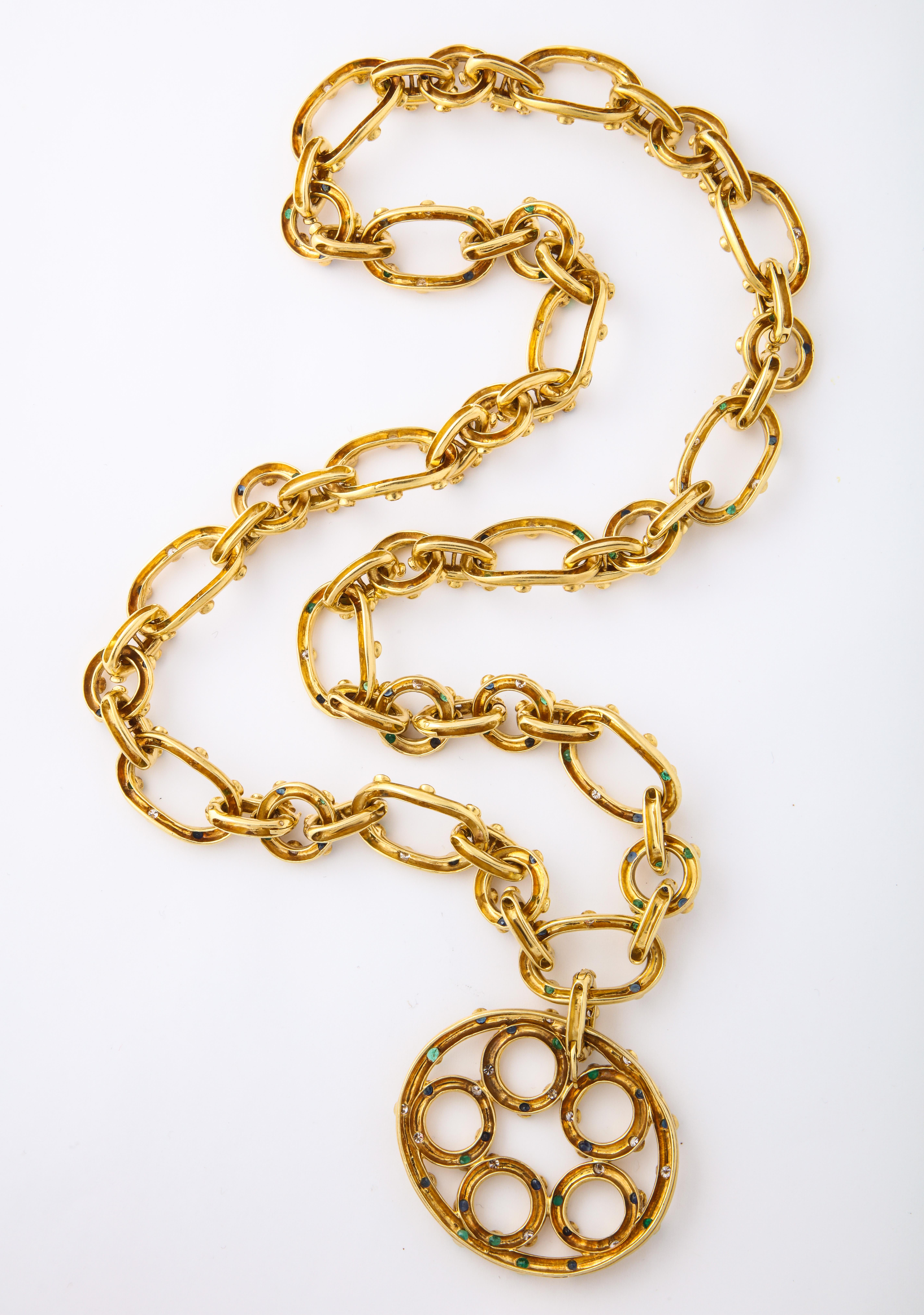 This stylish gold link necklace with a hanging pendant adorned with diamonds sapphires and emeralds.

A very chic 29 inches long

Depicted in full page spread in the 