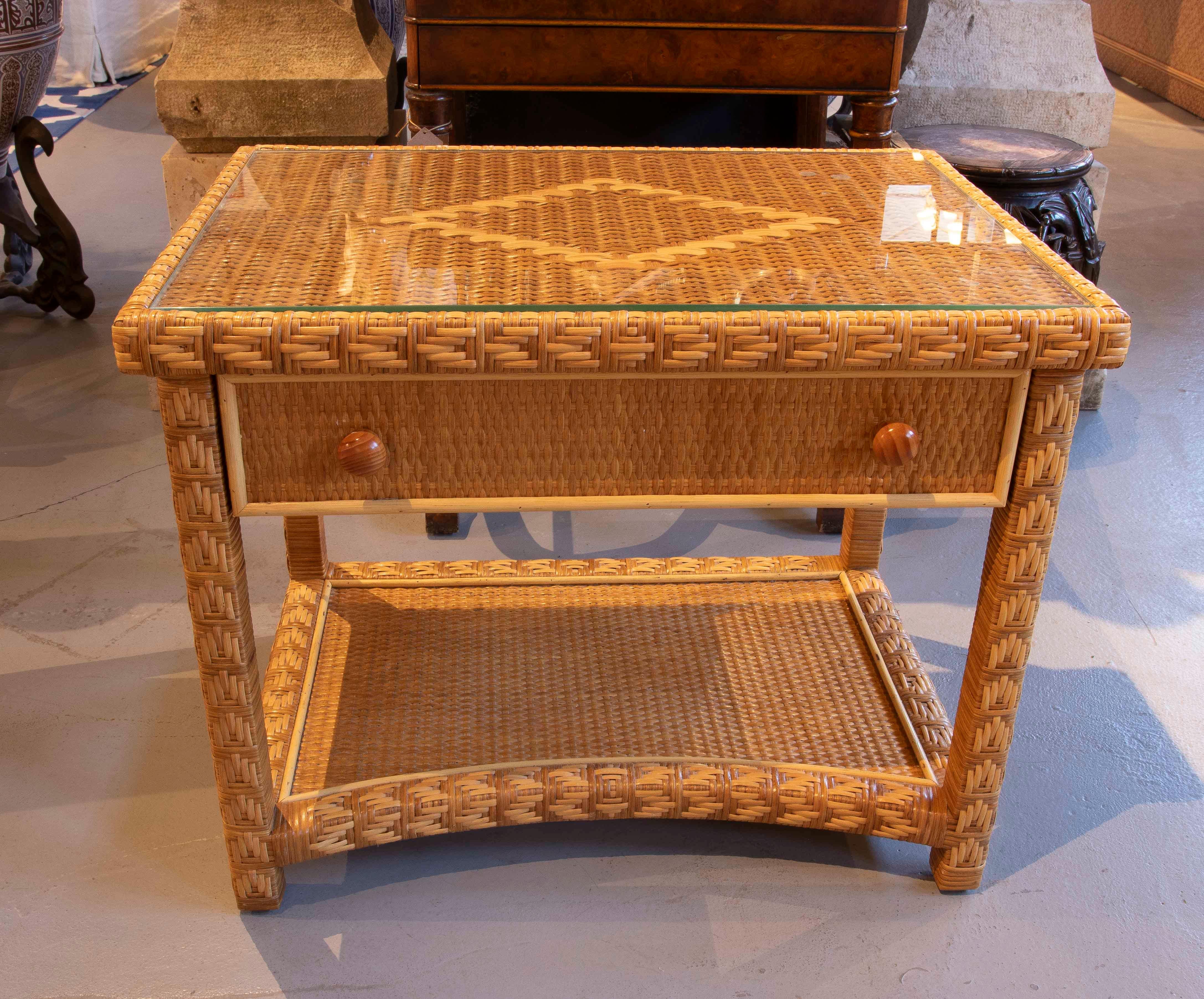 Charmanter Beistelltisch aus handgeflochtenem Naturrattan, mit verstärkter Struktur und dekorativen geometrischen Flechtdetails. Es verfügt über eine vordere Schublade mit Holzgriffen und eine praktische untere Ablage, die sich ideal zur