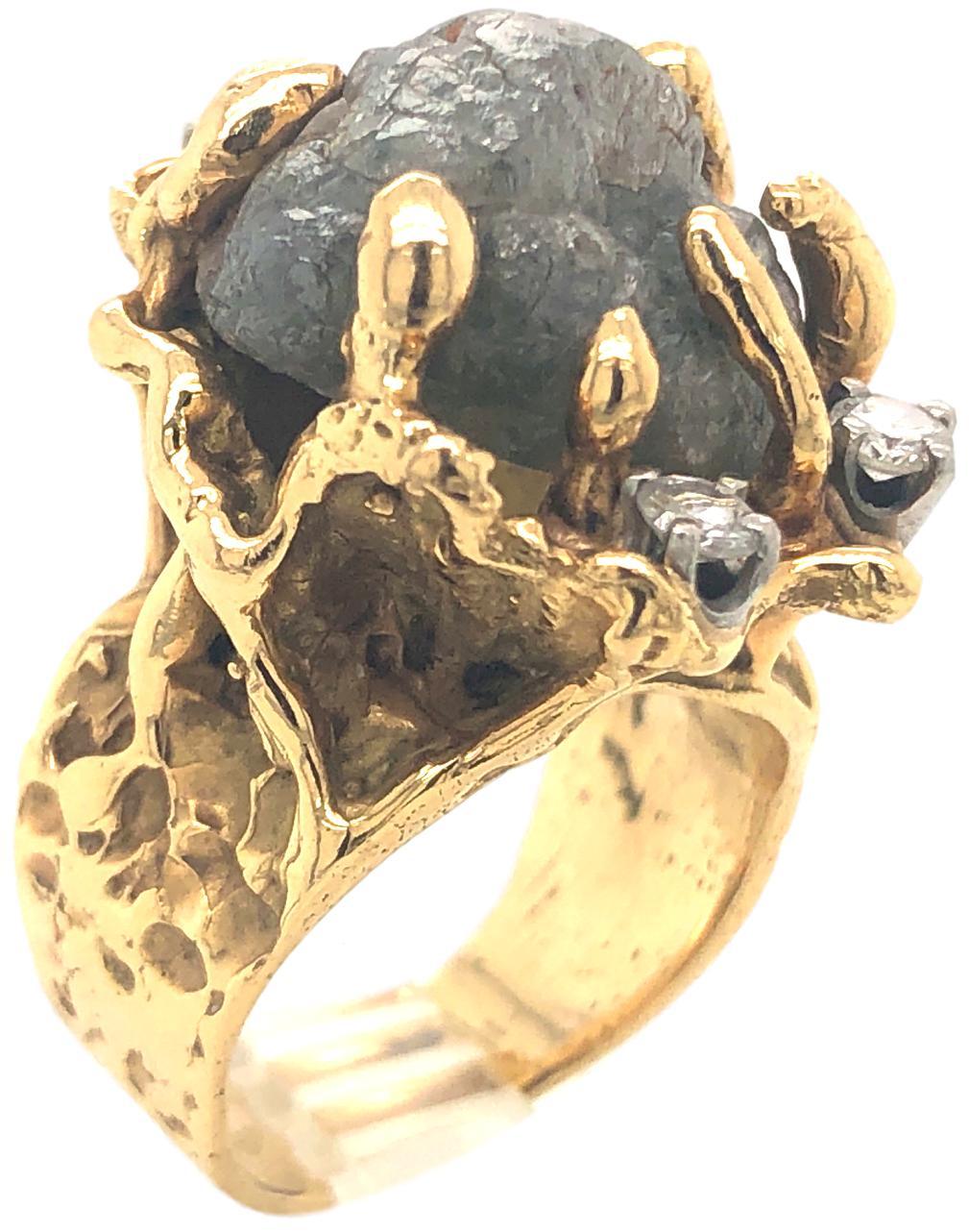 Brutalist vintage rough cut diamond ring. The 18k textured yellow gold ring with a medium grey, raw uncut diamond nugget weighing approximately 20cts, enhanced with three, round brilliant cut, white diamonds. . Not a 