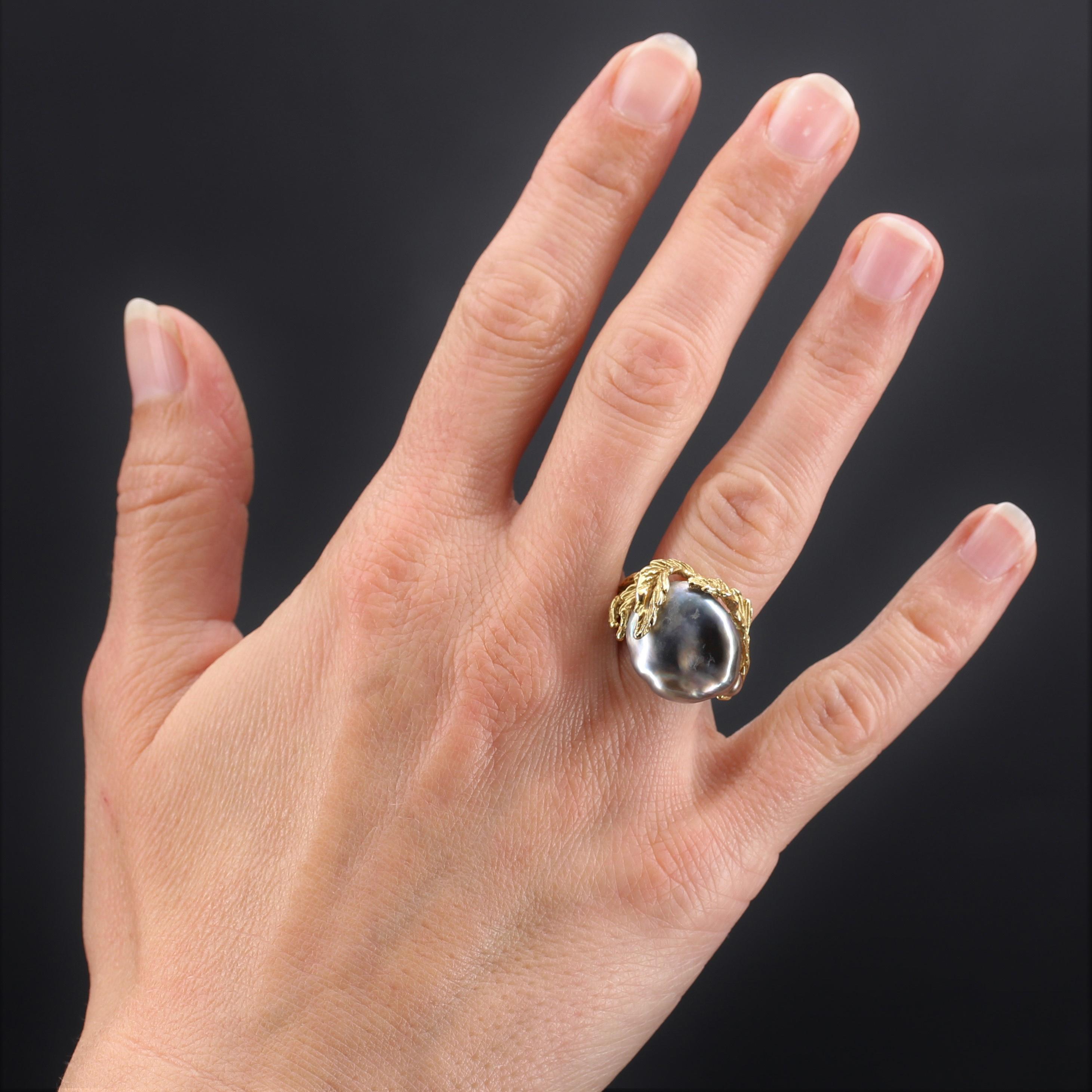 Ring in 18 karat yellow gold.
Incredible retro ring, it is formed of a setting stylizing a tree branch and its leaves that wrap around a large pearly anthracite grey baroque pearl.
Height : 18 mm approximately, width : 20.6 mm approximately,