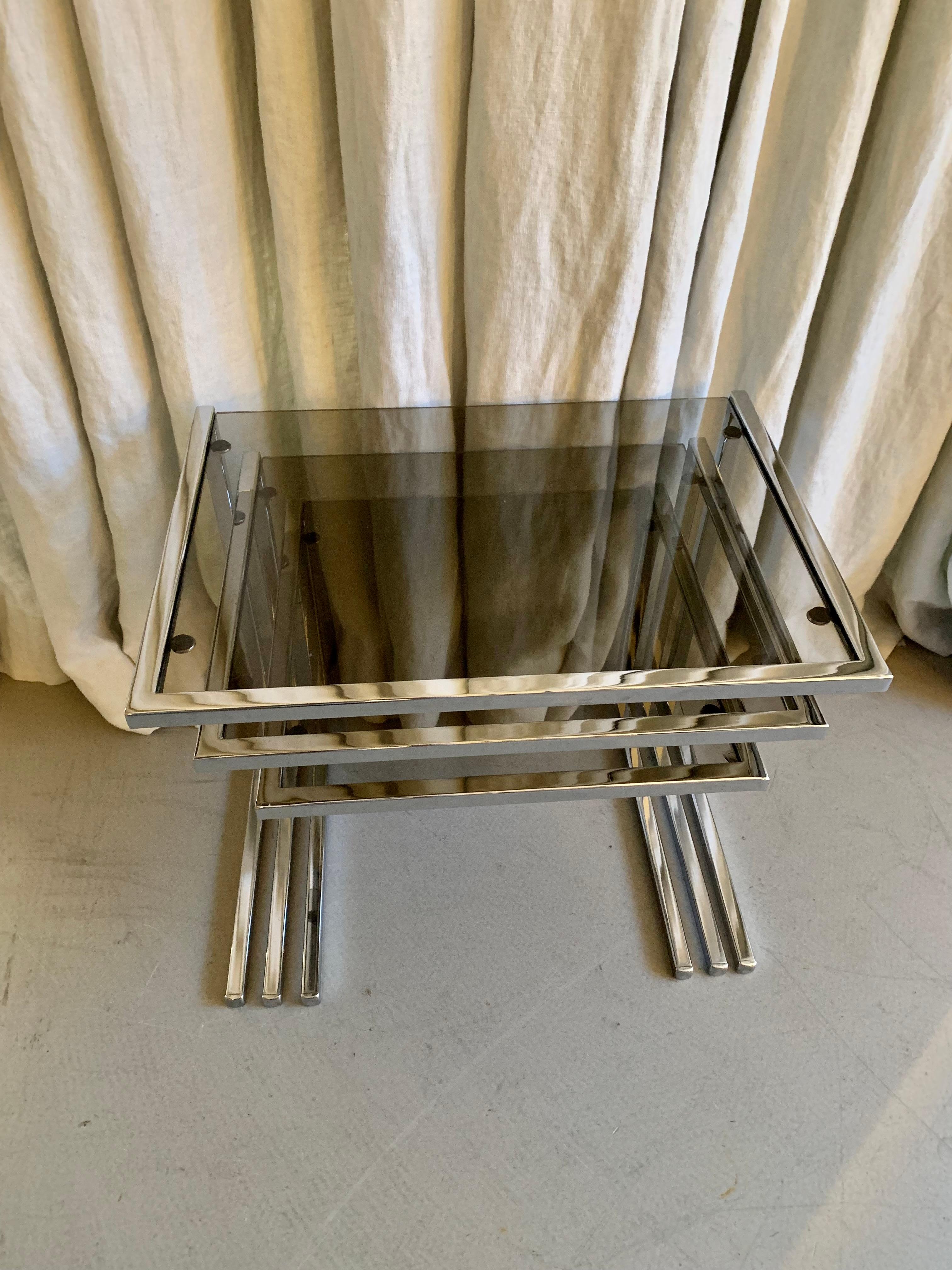Cool French vintage chrome and smoke colored glass nesting tables. The set of three is in good condition and has patina according to age and use.