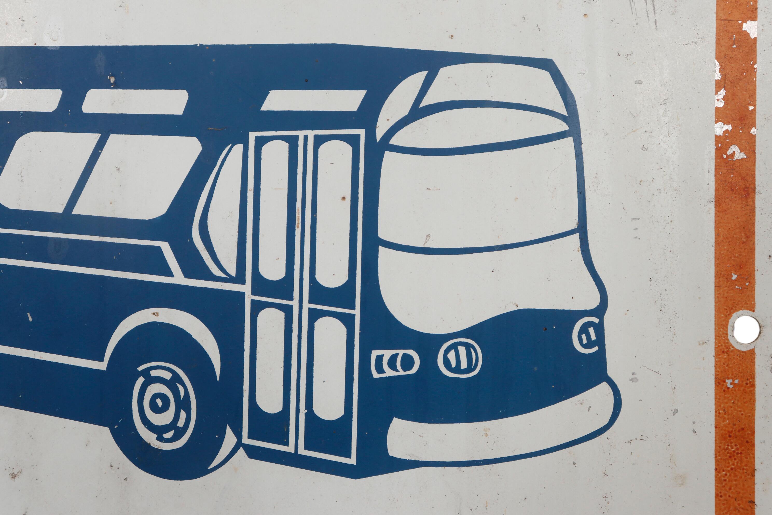 Panneau d'arrêt de bus new-yorkais des années 1970 en métal. Un bus art déco stylisé en bleu est placé dans un rectangle blanc au-dessus des mots 