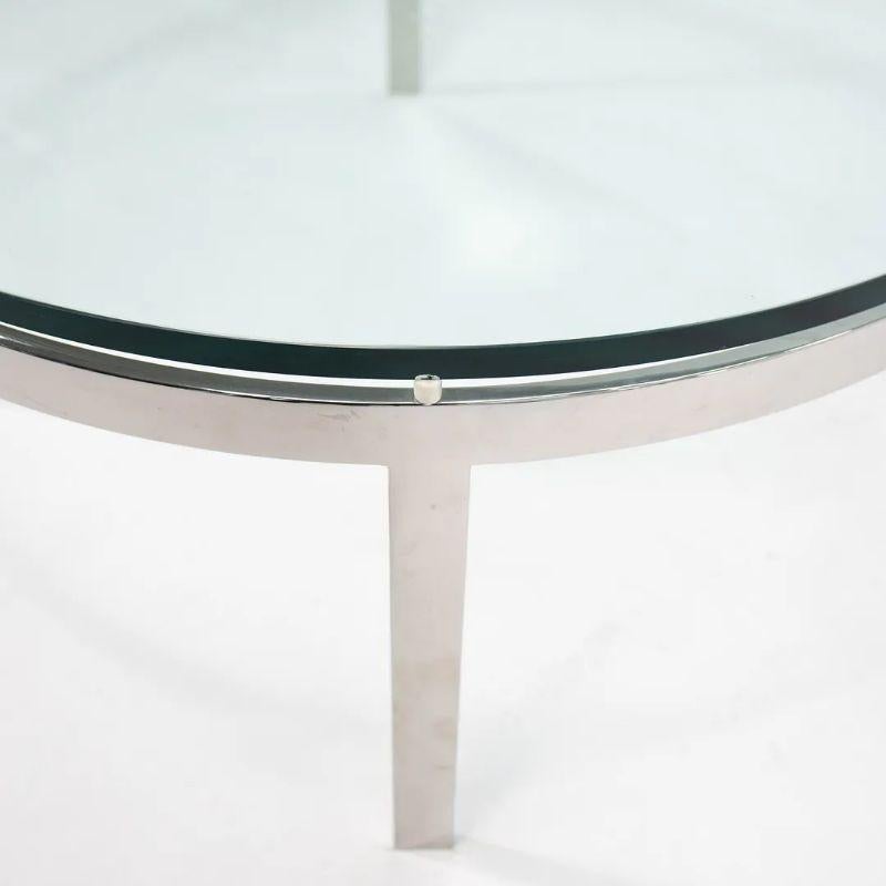 This is a round coffee table designed by Nicos Zographos and produced by Zographos Designs Ltd. circa 1970s. It has a thick tempered glass top with polished stainless steel base. The base is generally in very good to excellent vintage condition. The