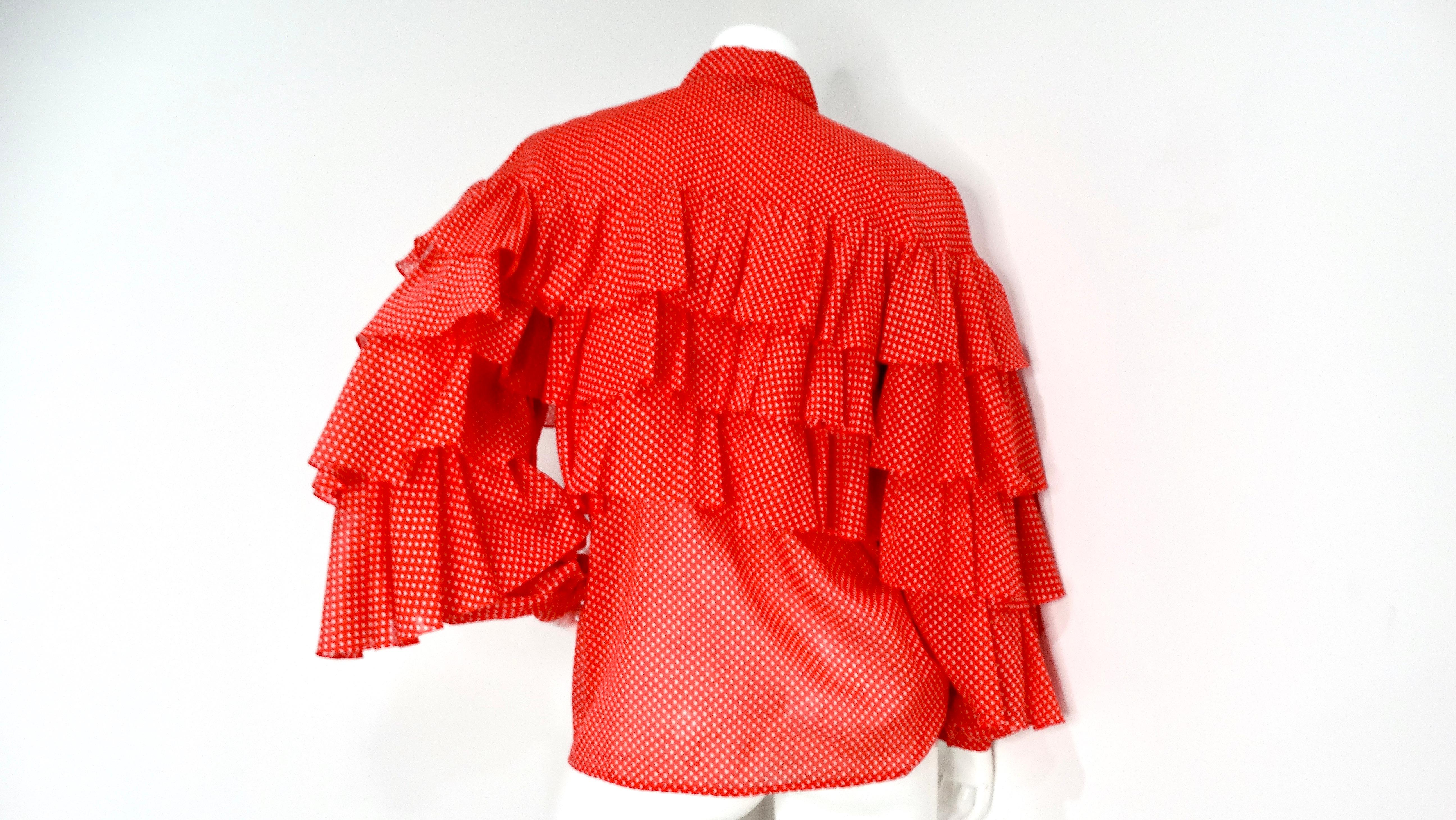 This vintage Nina Ricci blouse captures the playful elegance of the 1970s. The vibrant orange-red hue serves as a striking backdrop for crisp white polka dots, creating a visually appealing and energetic design. The blouse features a high, buttoned