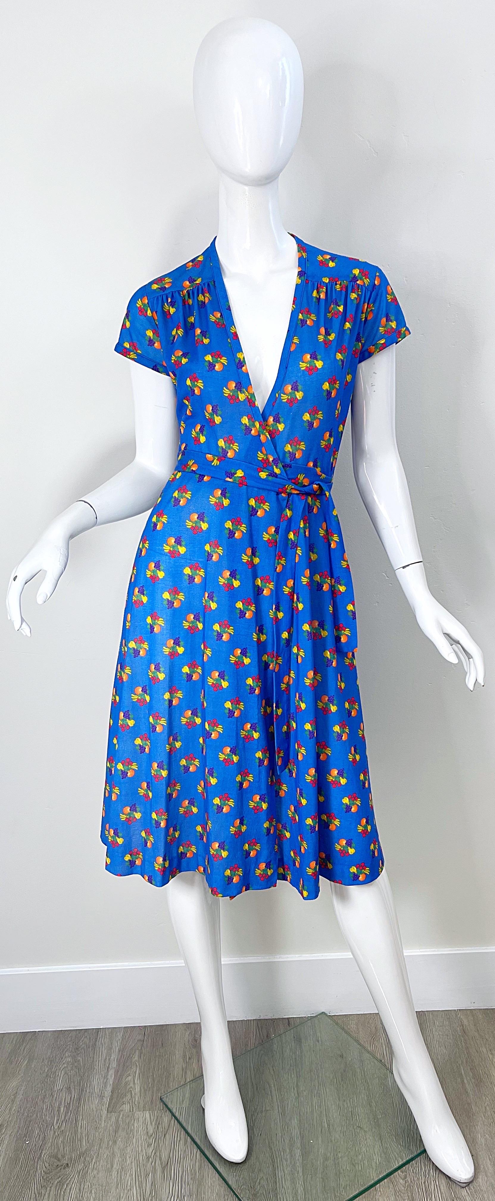 Superbe robe portefeuille de la fin des années 70 à imprimé fruits ! Le fond est d'un beau bleu vibrant. Des impressions de raisins violets, de citrons et de poires jaunes, d'oranges et de framboises sont omniprésentes. L'attache à la taille