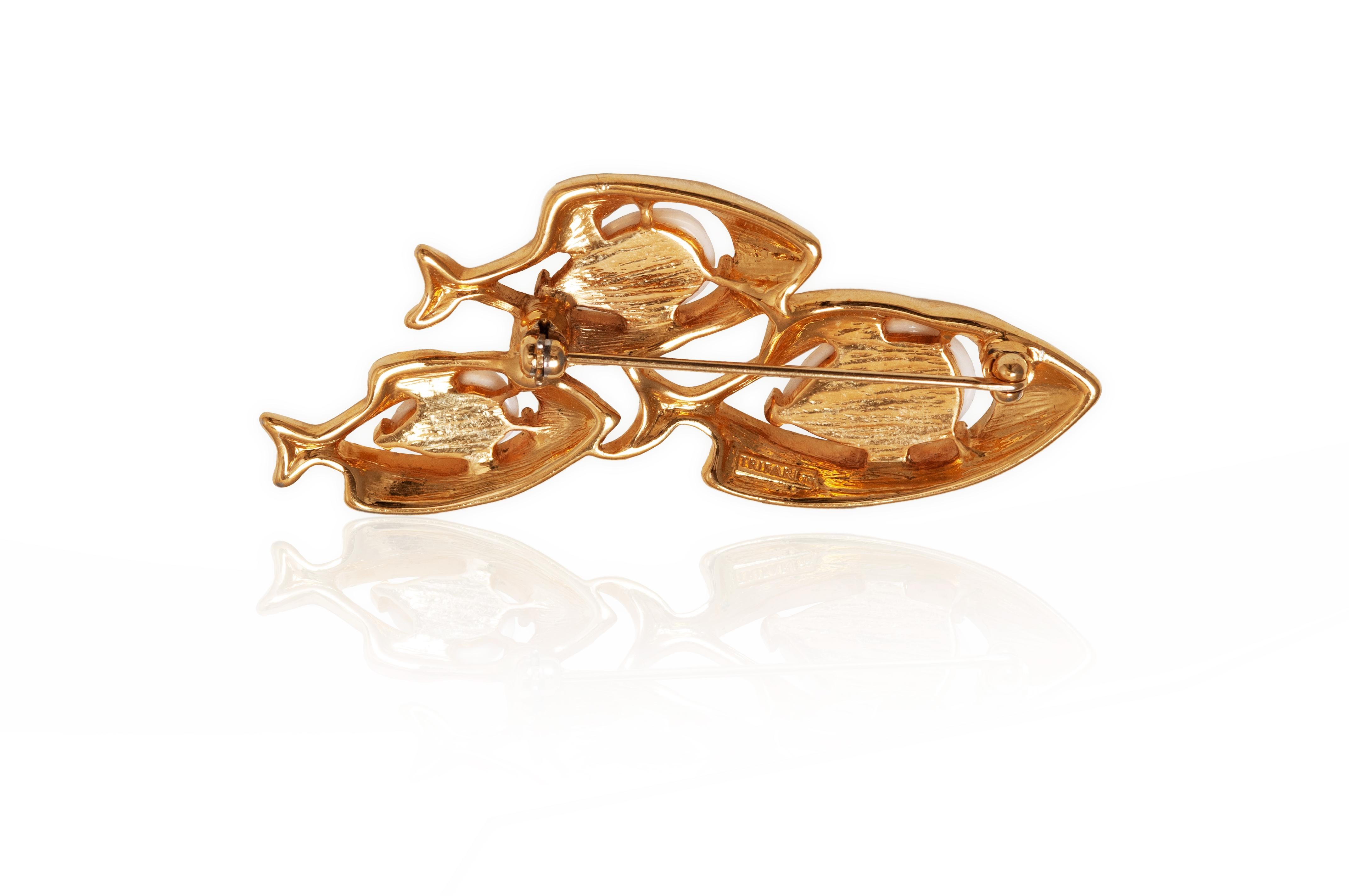 1970s Trifari brooch in the form of 3 fish swimming in a school with a larger fish followed by 2 smaller ones. The fish are made of gold tone metal with their bodies comprised of white moulded glass. The brooch has the mark Trifari TM stamp on the