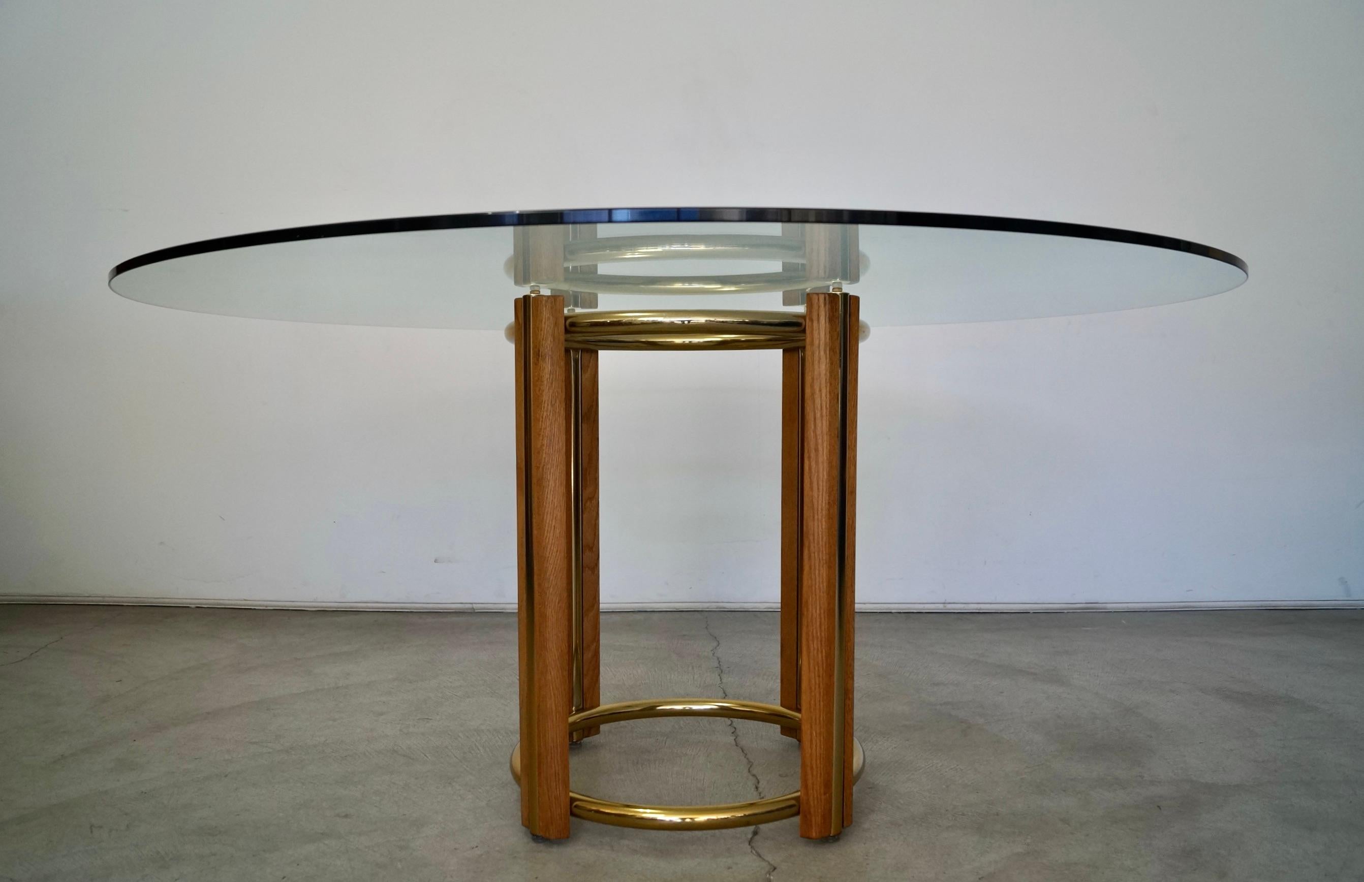 Vintage 1970s Mid-Century Modern dining table for sale. Has a solid oak base with brass rings and brass inserted into the oak. The has a half inch thick large round glass top. This table is in incredible condition. The glass has no chips and looks