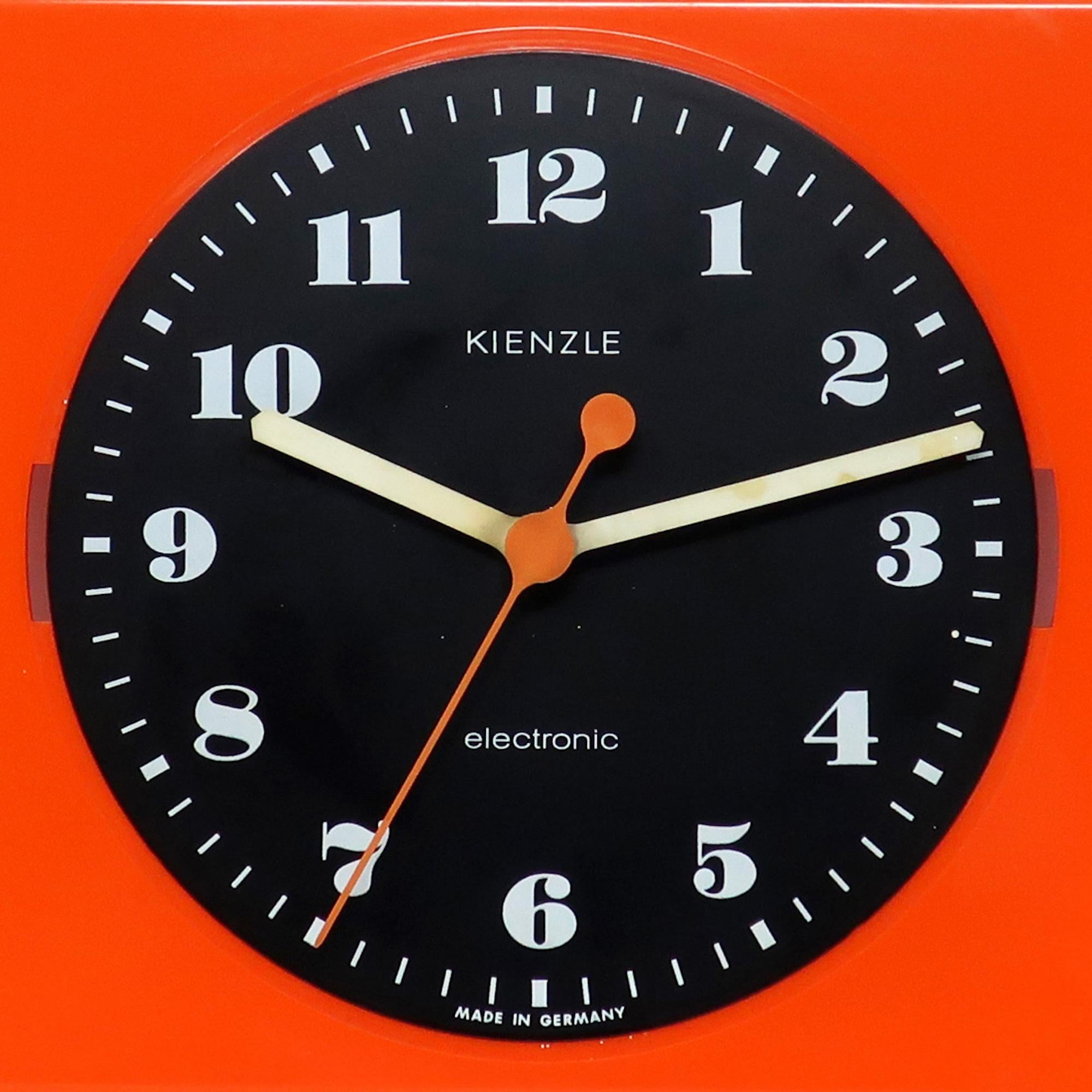 A vintage mid-century modern orange, black, and white Electronic wall clock by German clock manufacturer Kienzle. Body of this Space Age clock is orange plastic, the face is black, and the numbers and hands are white, all of which provides a