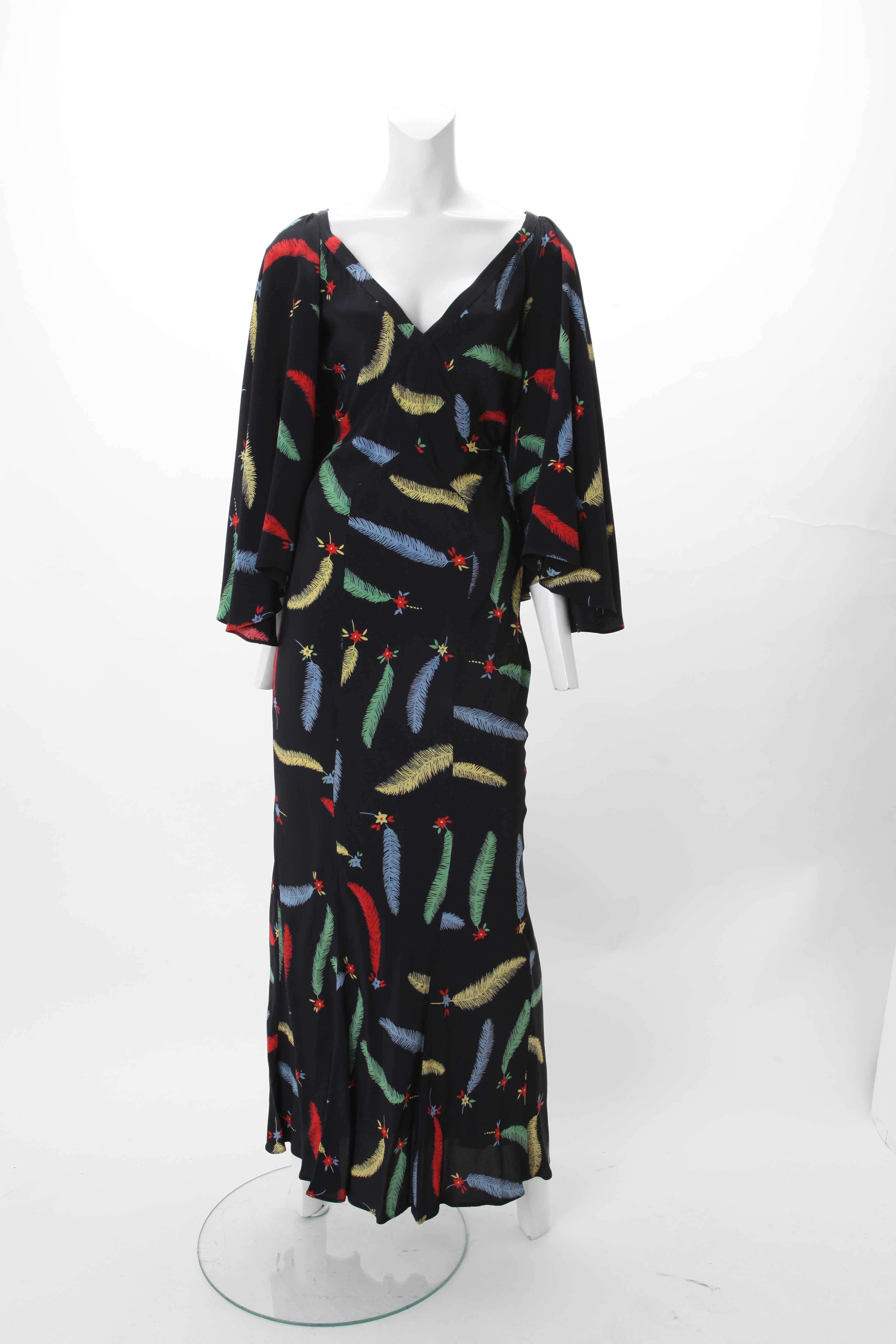 1970s Ossie Clark Celia Birtwell Print Maxi Gown; V-neck empire bodice with flared sleeves; Open back with criss-cross panels w/ metal hoop fastening; side zipper closure. Polychrome leaf and flowerhead print on black ground.