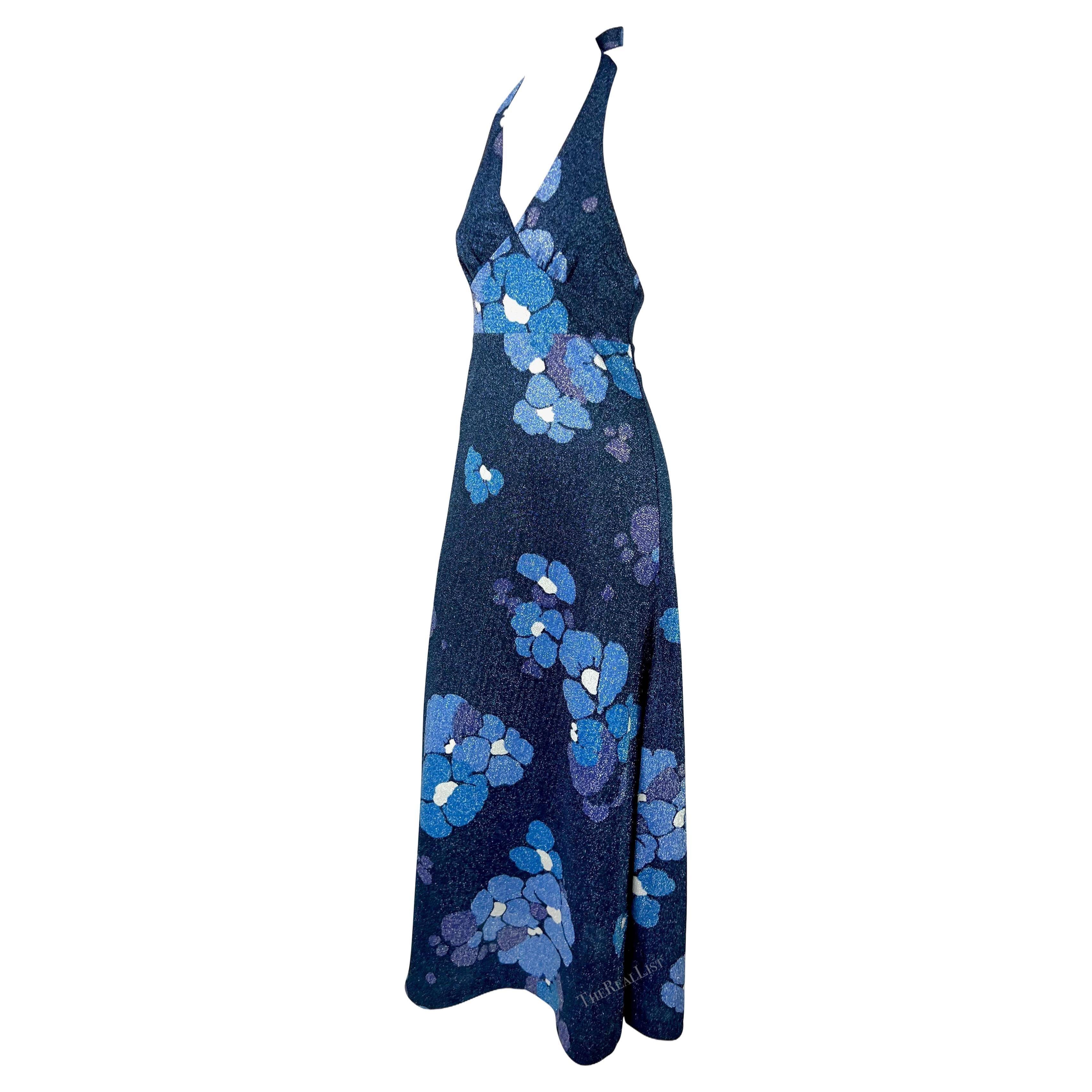 Te presentamos un deslumbrante vestido azul floral Paco Rabanne de cuello haltern de los años 70. Este luminoso vestido de lúrex luce un estampado floral azul metálico en toda su superficie. Su diseño de largo hasta el suelo incluye un profundo