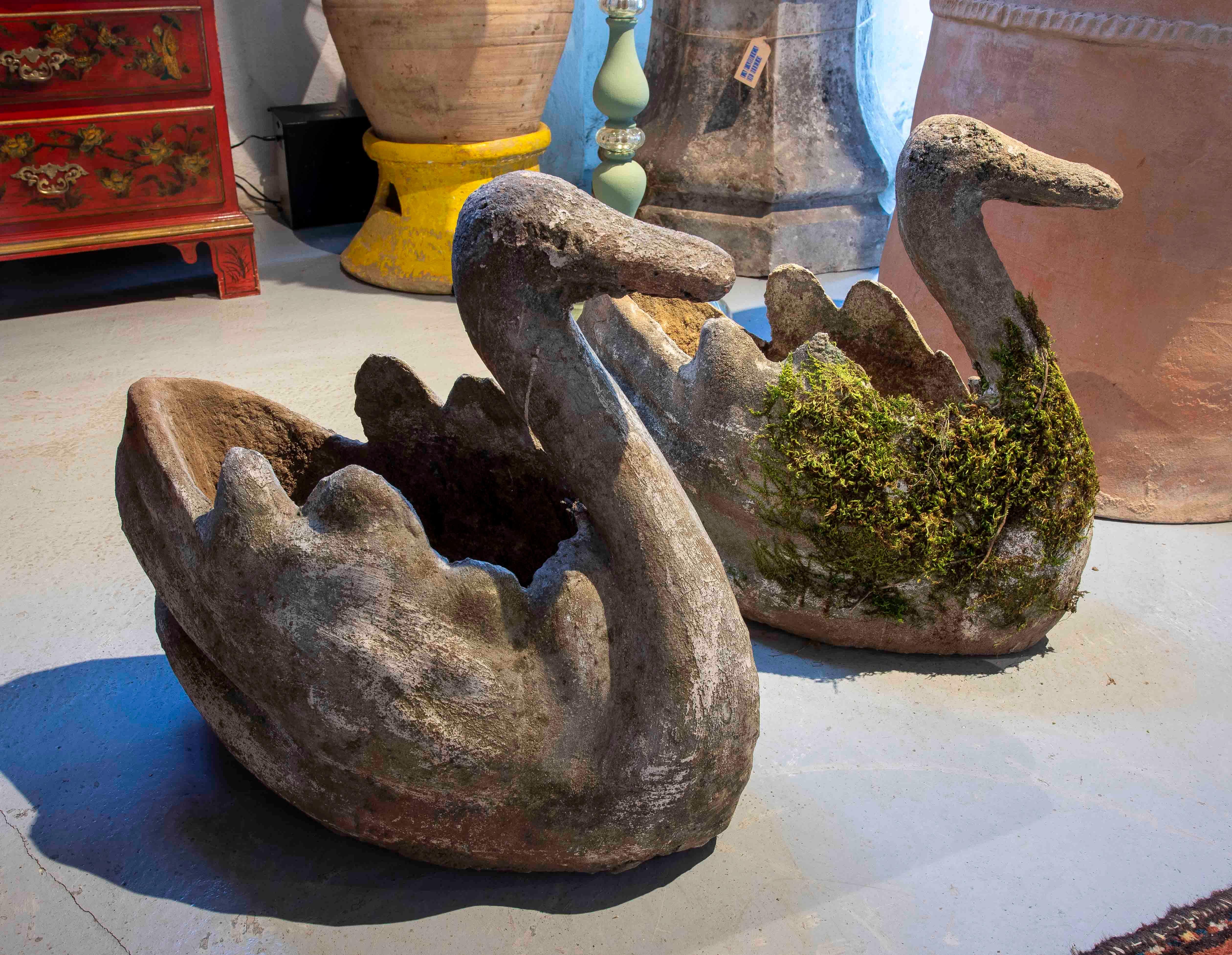 Un'affascinante coppia di fioriere antiche a forma di cigno, realizzate in pietra con una finitura invecchiata che aggiunge un tocco rustico e naturale. Il loro design dettagliato, con texture che imitano le piume e un elegante collo curvo,