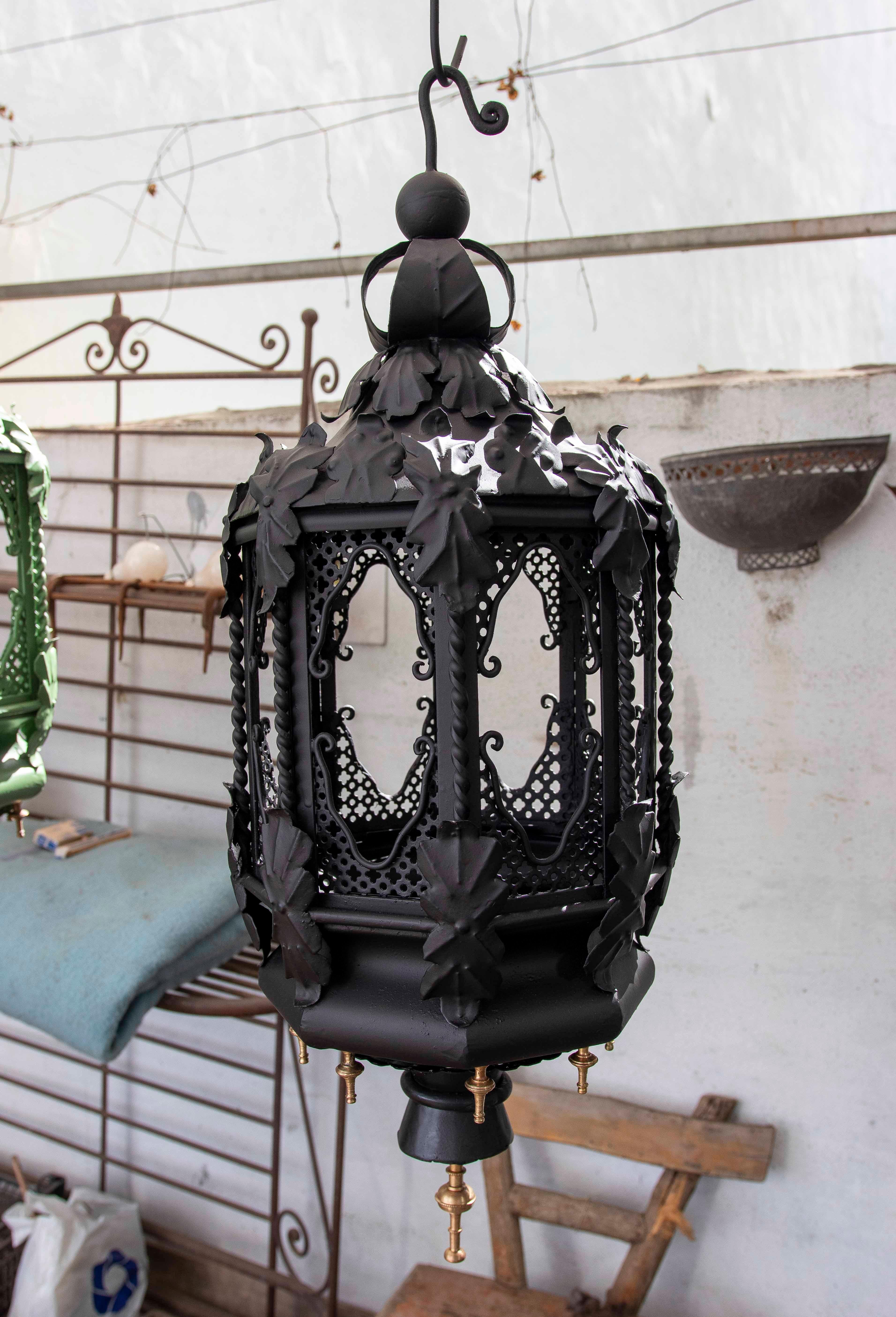 Un'elegante coppia di lampade a sospensione in ferro battuto di colore nero opaco, con un design elegante e decorato. Ogni lampada presenta dettagli traforati e decorazioni a forma di foglia, evocando uno stile classico e sofisticato. La sua