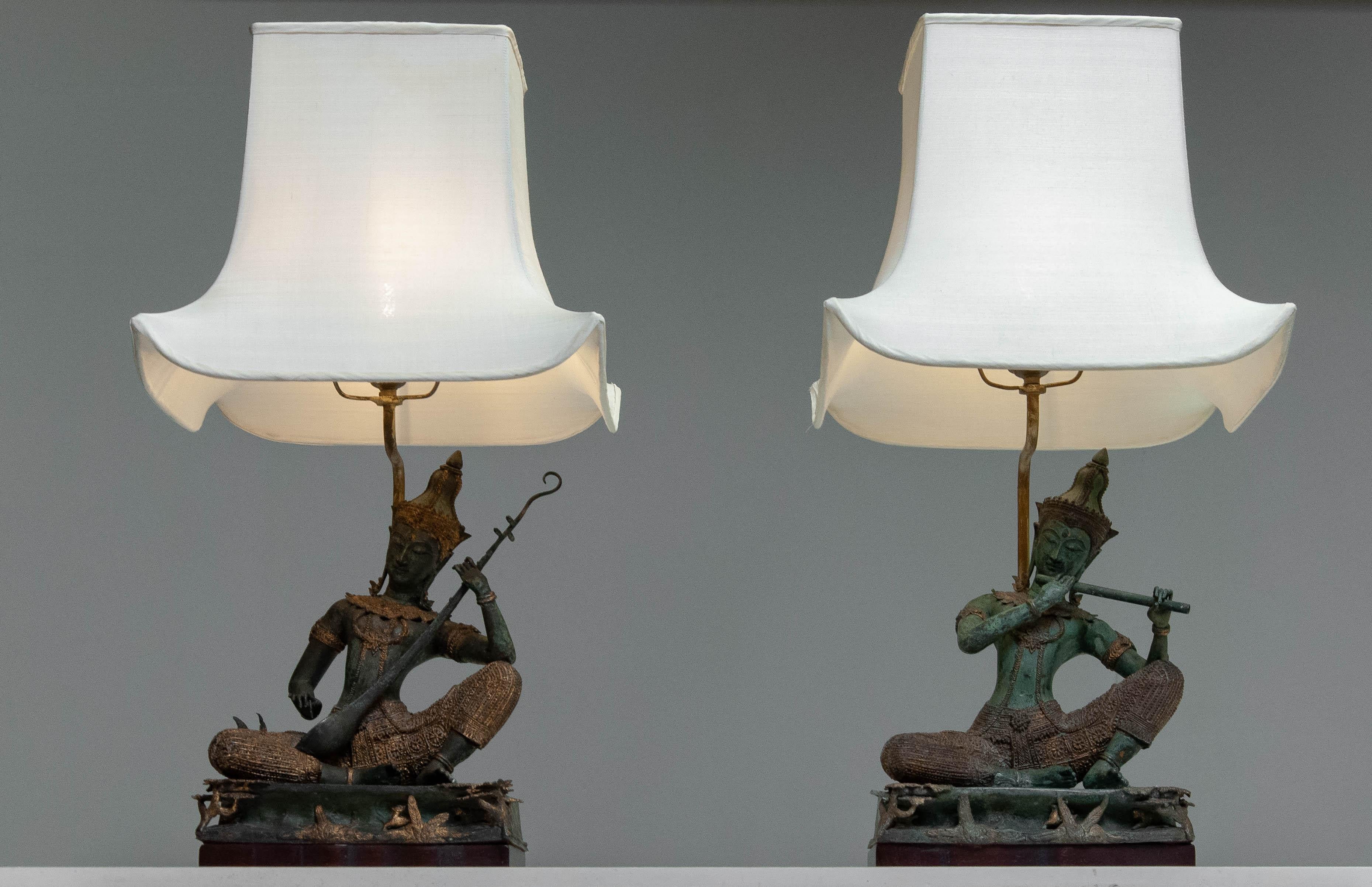 Superbe ensemble de deux lampes de table en bronze représentant des figures de musiciens thaïlandais assis, aux détails complexes.

MATERIAL : Bronze coulé avec détails dorés
Design/One : Divinités traditionnelles inspirées de l'Asie du Sud-Est,