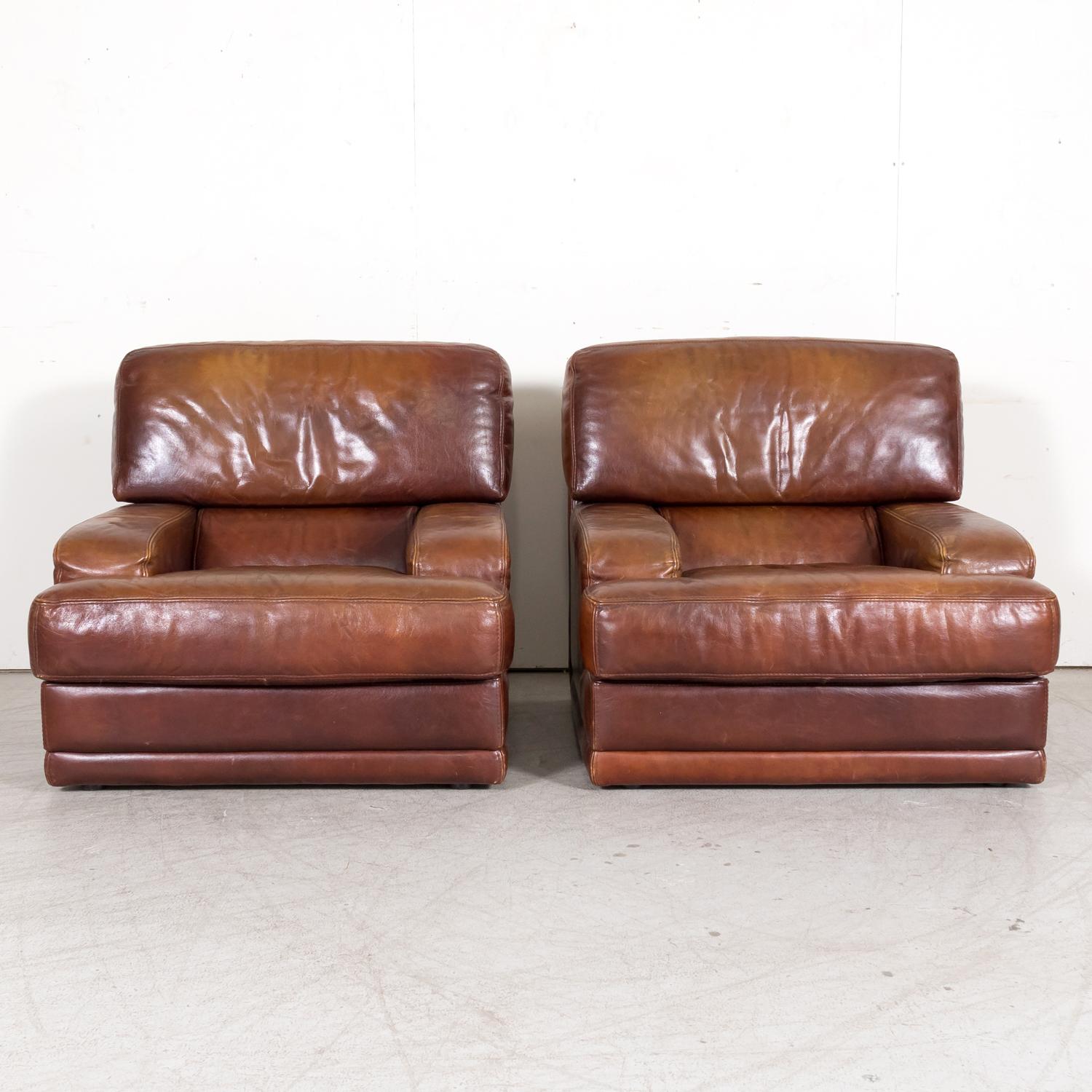 A pair of late 20th century mid-century modern French oversized patinated cognac leather lounge chairs, circa 1970s. These fabulous vintage leather armchairs, with their contemporary lines, are making serious function out of fashion! Both stylish