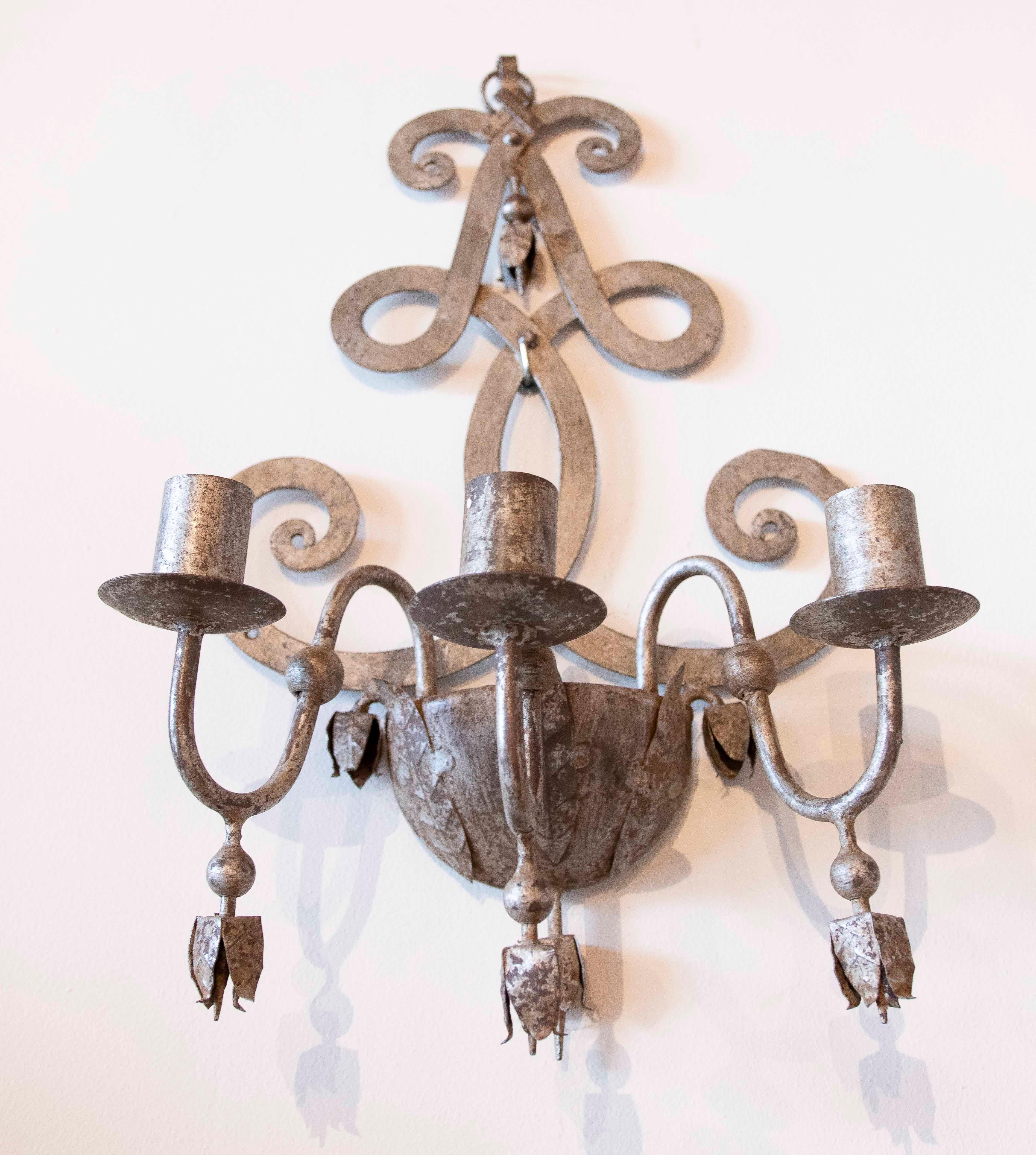 Elegante coppia di appliques in ferro battuto con finitura invecchiata che ne evidenzia lo stile classico e senza tempo. Ogni applique presenta un design decorativo con curve ornamentali e tre portacandele, ideali per creare un'atmosfera calda e