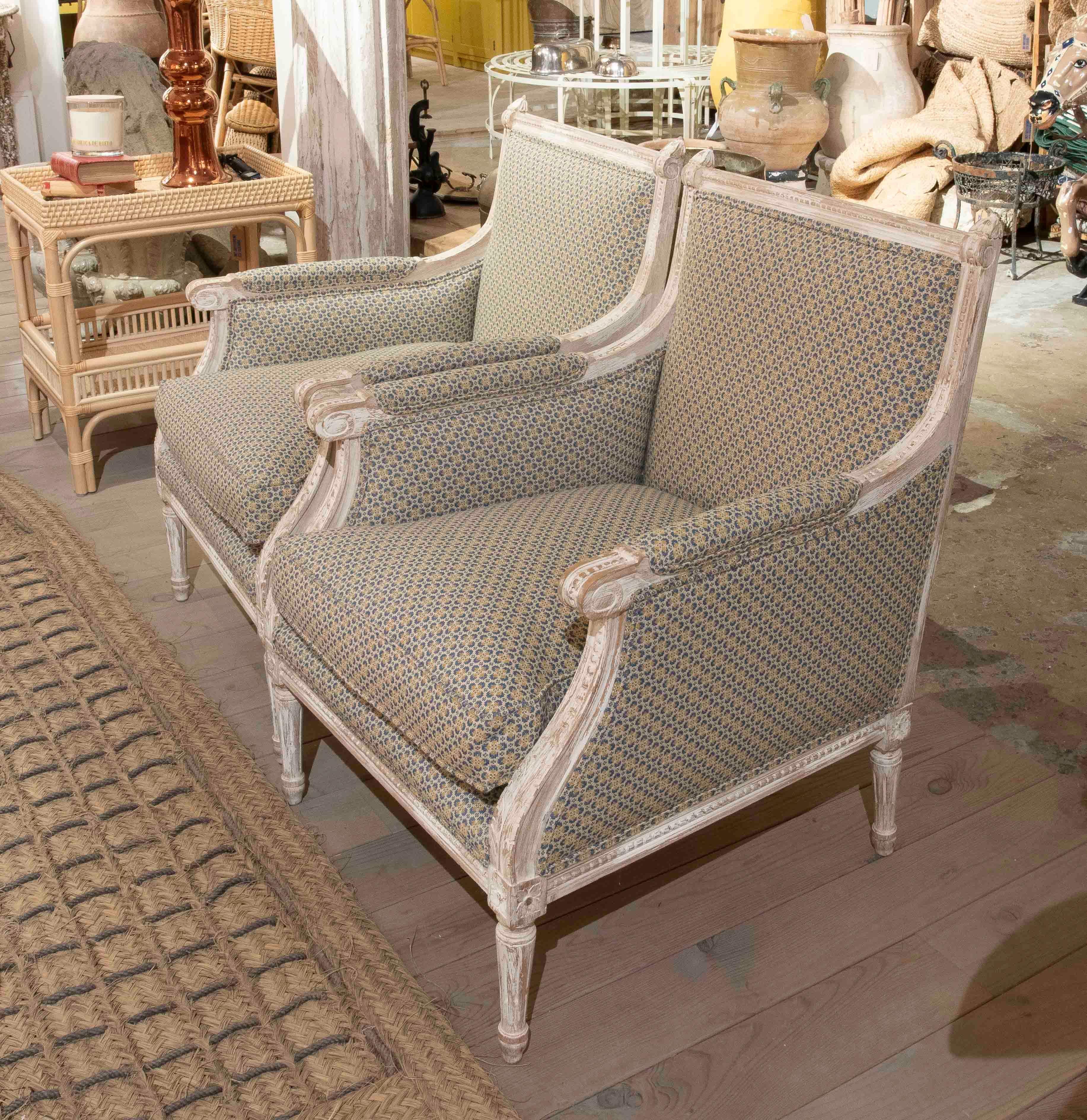 Ein elegantes Paar Sessel im Louis XVI-Stil mit einem geschnitzten Holzrahmen, der in einem gealterten Cremeton lackiert ist. Die geschwungenen Armlehnen, die geriffelten Beine und die geometrische Polsterung in Blau- und Senftönen vereinen Komfort