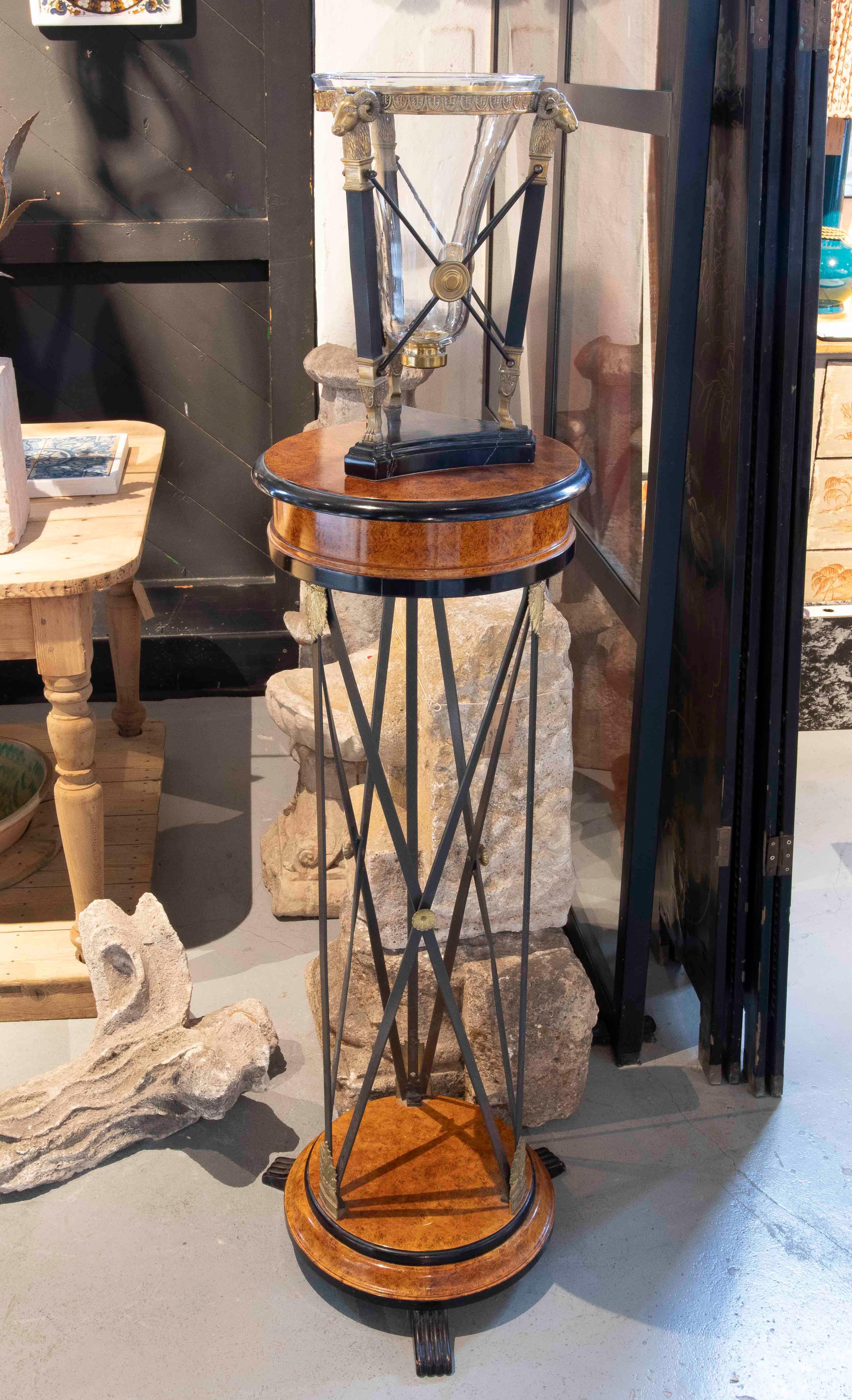 An elegant pair of neoclassical columns or pedestals, ideal for displaying sculptures, vases, or decorative pieces. Each pedestal combines a circular wooden base with warm grain and a structural system of interwoven iron, enhanced with decorative