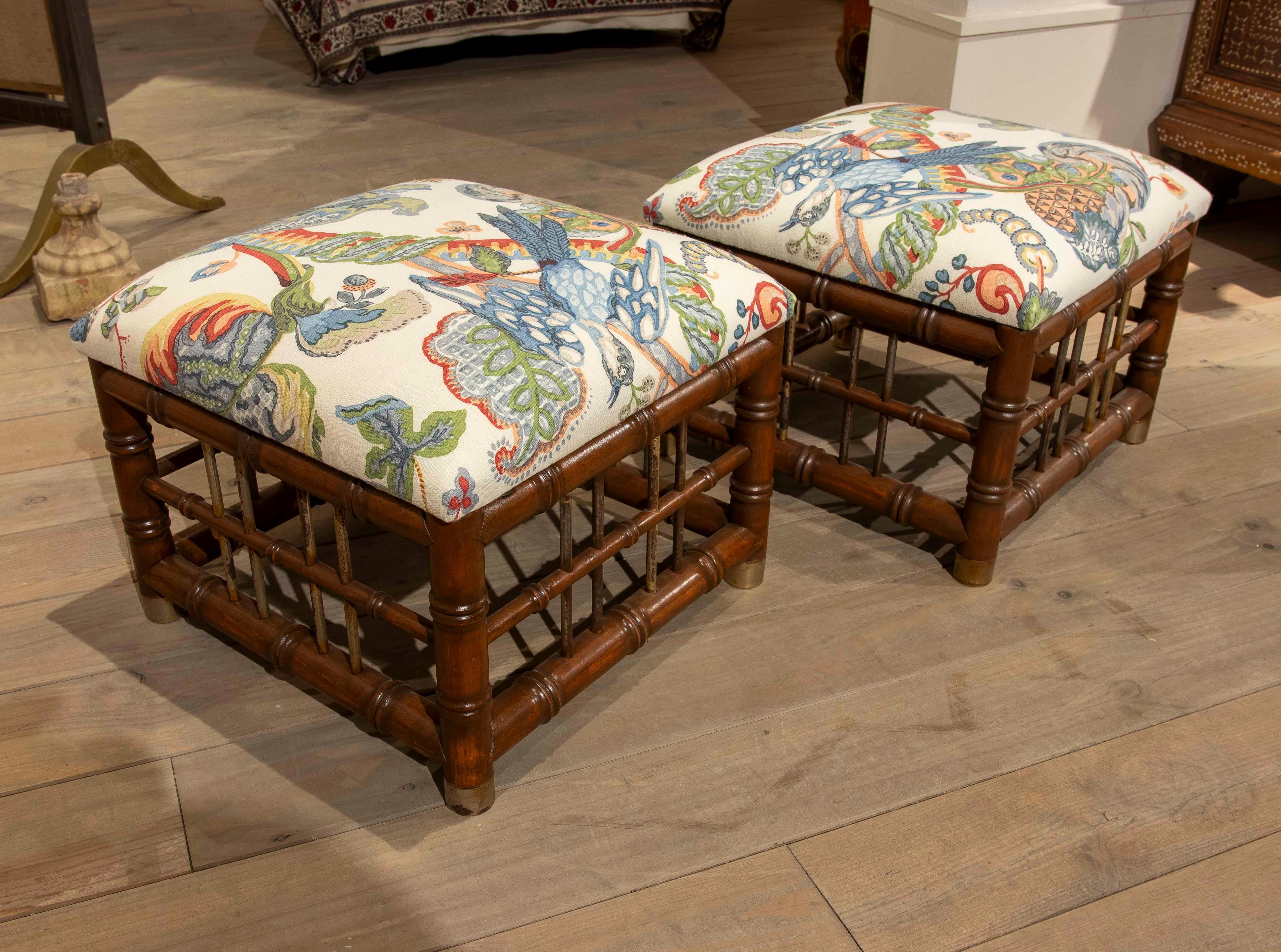 Un ensemble de deux tabourets avec une structure en bambou tourné, apportant chaleur et texture visuelle. L'assise est recouverte d'un tissu de couleur claire avec un imprimé coloré d'inspiration tropicale comprenant des oiseaux, des ananas et du