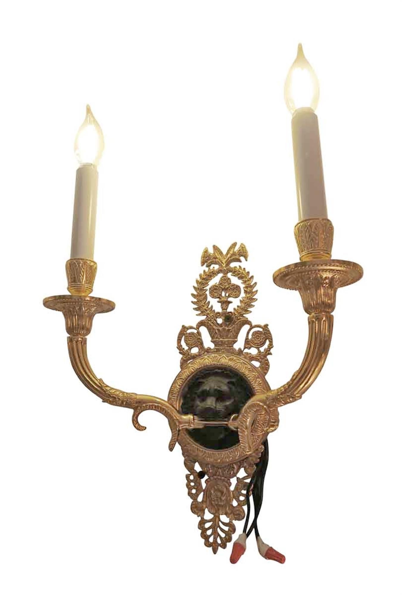 Pair of heavy cast brass 20th century two-arm candlestick sconces with black lion faces in the center of the back plate and gold gilt finished details. These adorned several suites of the Waldorf Astoria Hotel. Priced as a pair. Waldorf Astoria