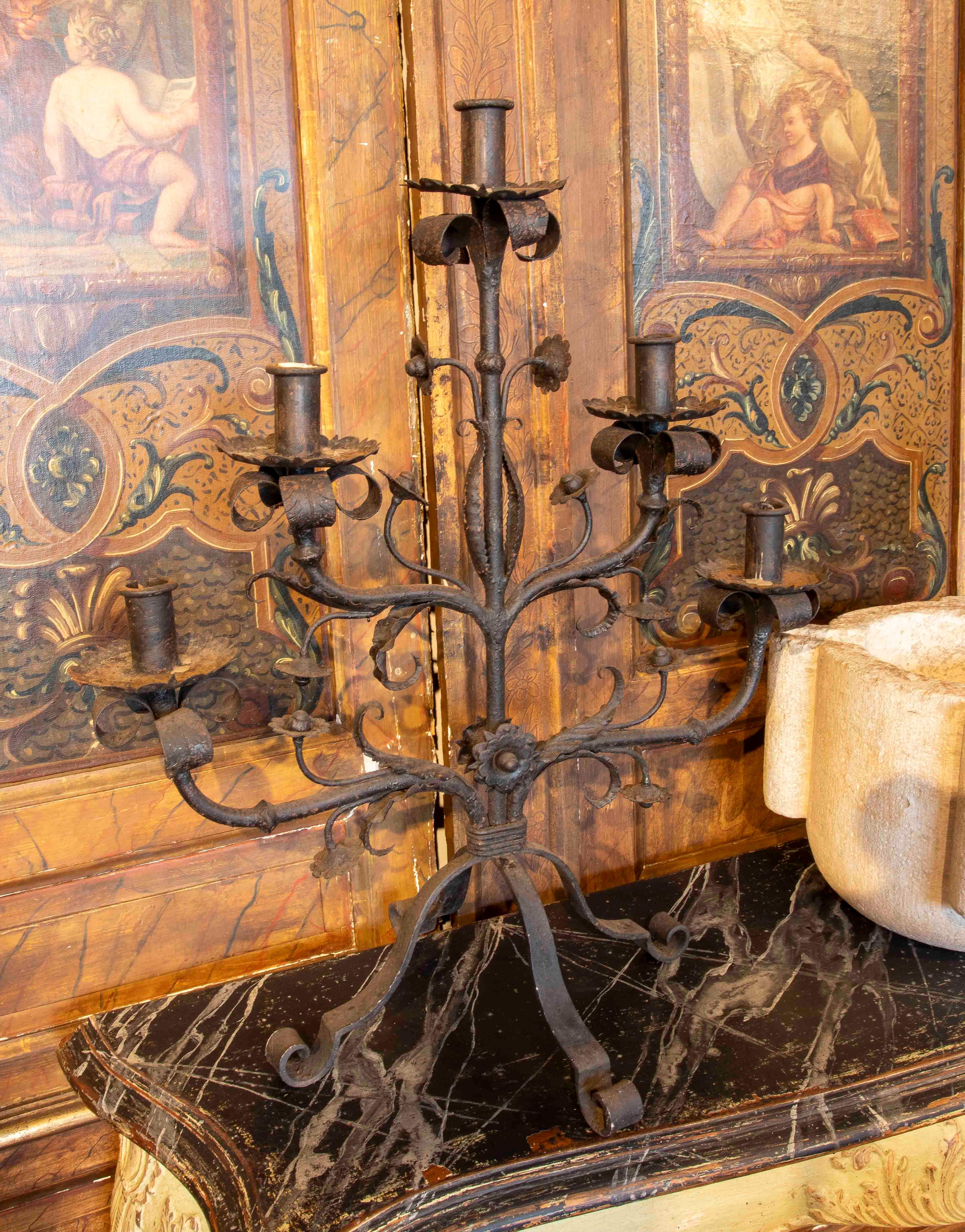 Magnífica pareja de candeleros de mesa de hierro forjado, cada uno con cinco brazos de candelero. Presentan un diseño orgánico con ramas curvadas y hojas decorativas martilladas a mano, que evocan un estilo gótico o rústico español. La base en forma