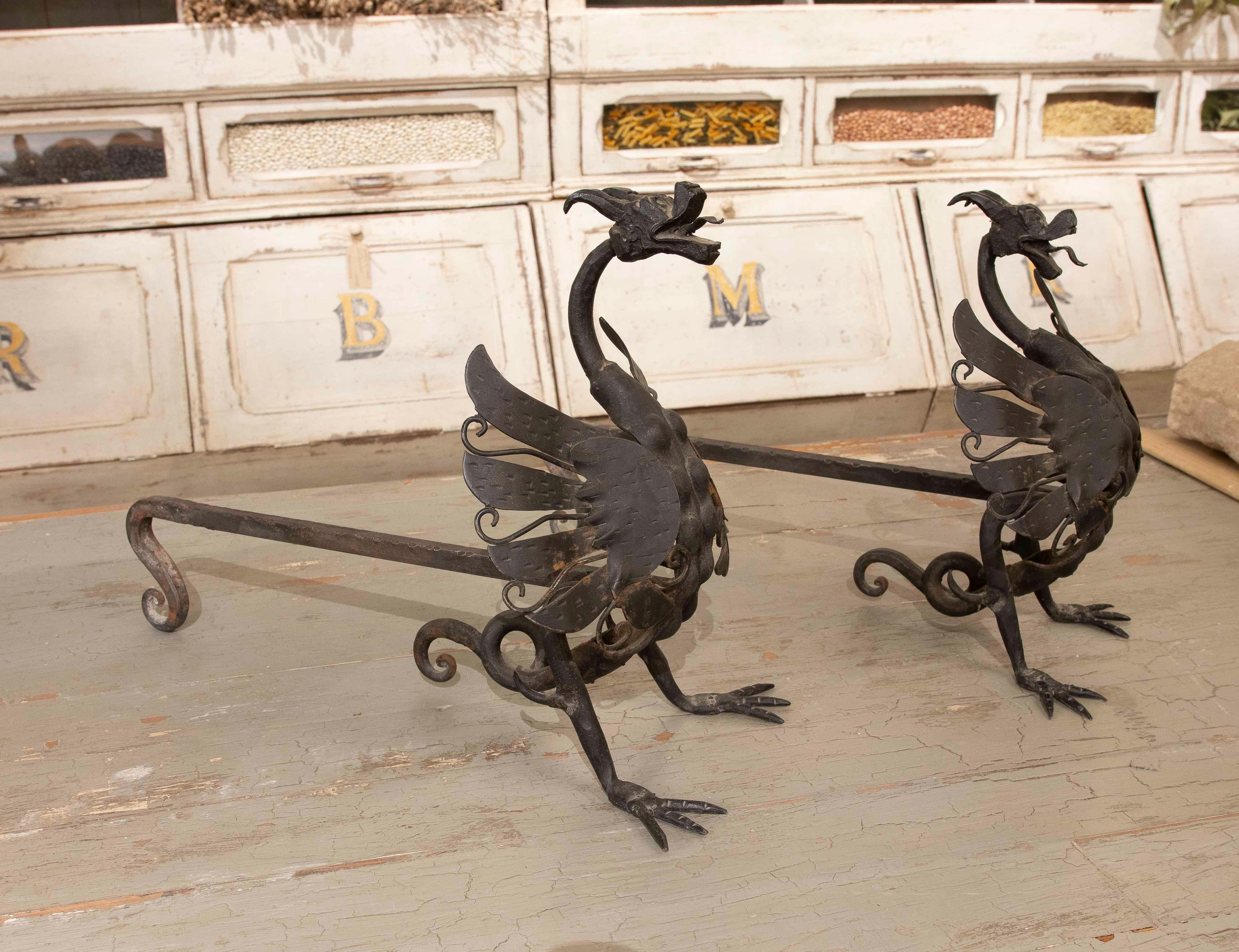 Set di due candelabri per caminetto in ferro battuto, raffiguranti figure dettagliate di draghi con ali stilizzate e teste espressive. Questo design unico combina funzionalità e impatto visivo, ideale per aggiungere carattere e stile a caminetti