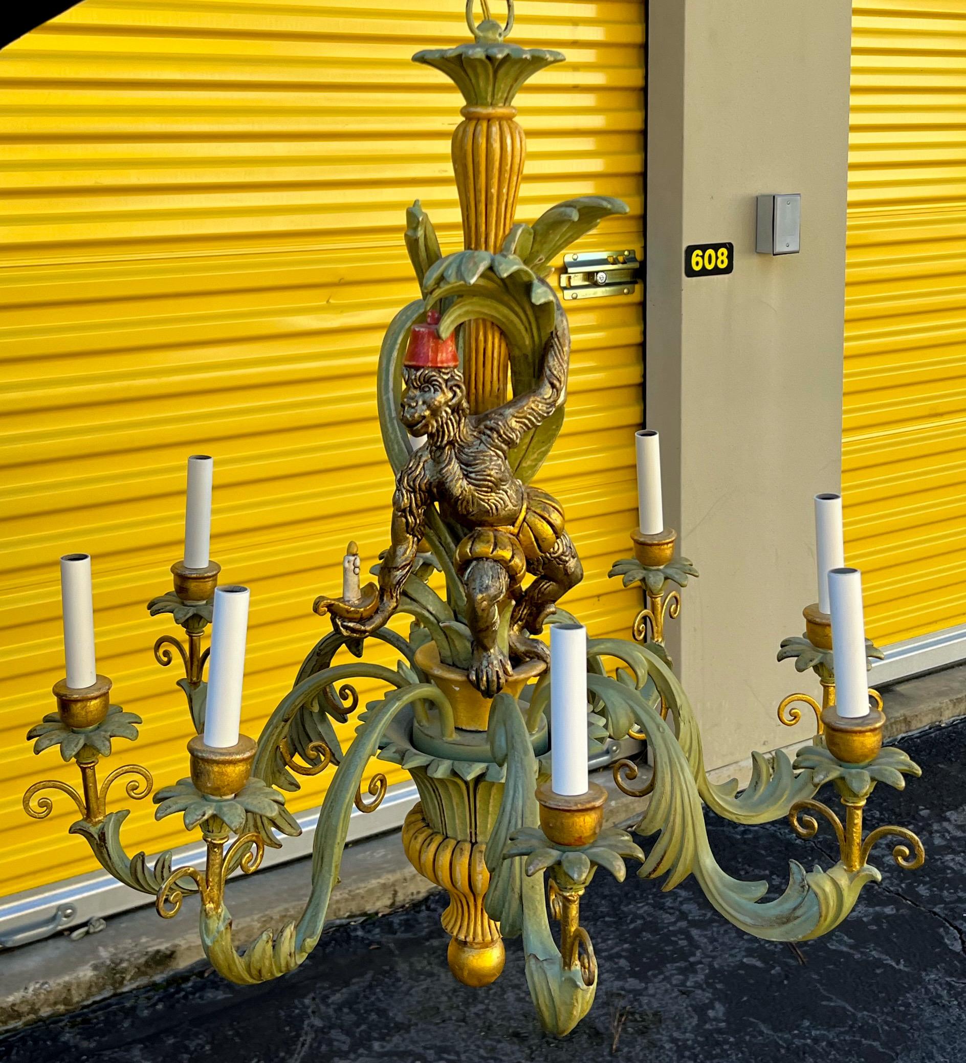 This is a Regency style 1970s carved wood chandelier depicting a monkey holding onto the stem with a candle in his hand. It has 8 arms and is in very good condition.