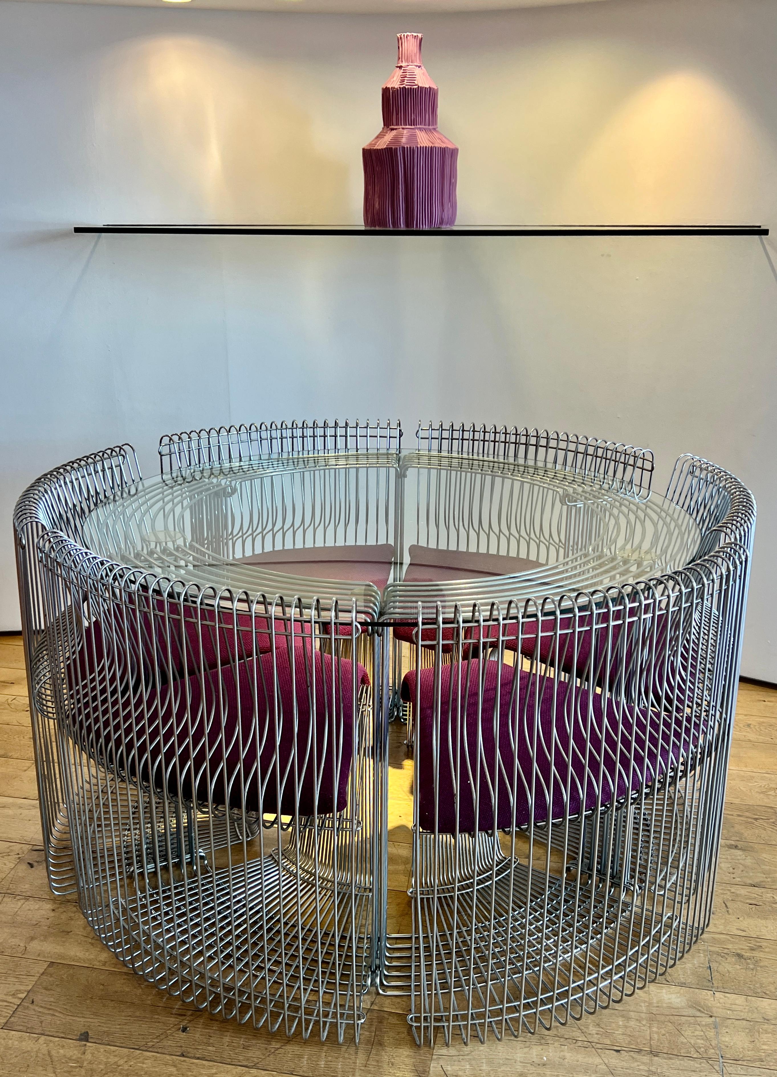 Designed 1971, for Fritz Hansen, Denmark
Chrome-plated steel with glass top. Six chairs slide underneath, each with its original textured aubergine seat pad secured by small plastic hooks. (Seat cushions are removable)..
Table ⌀ 121 / H 70