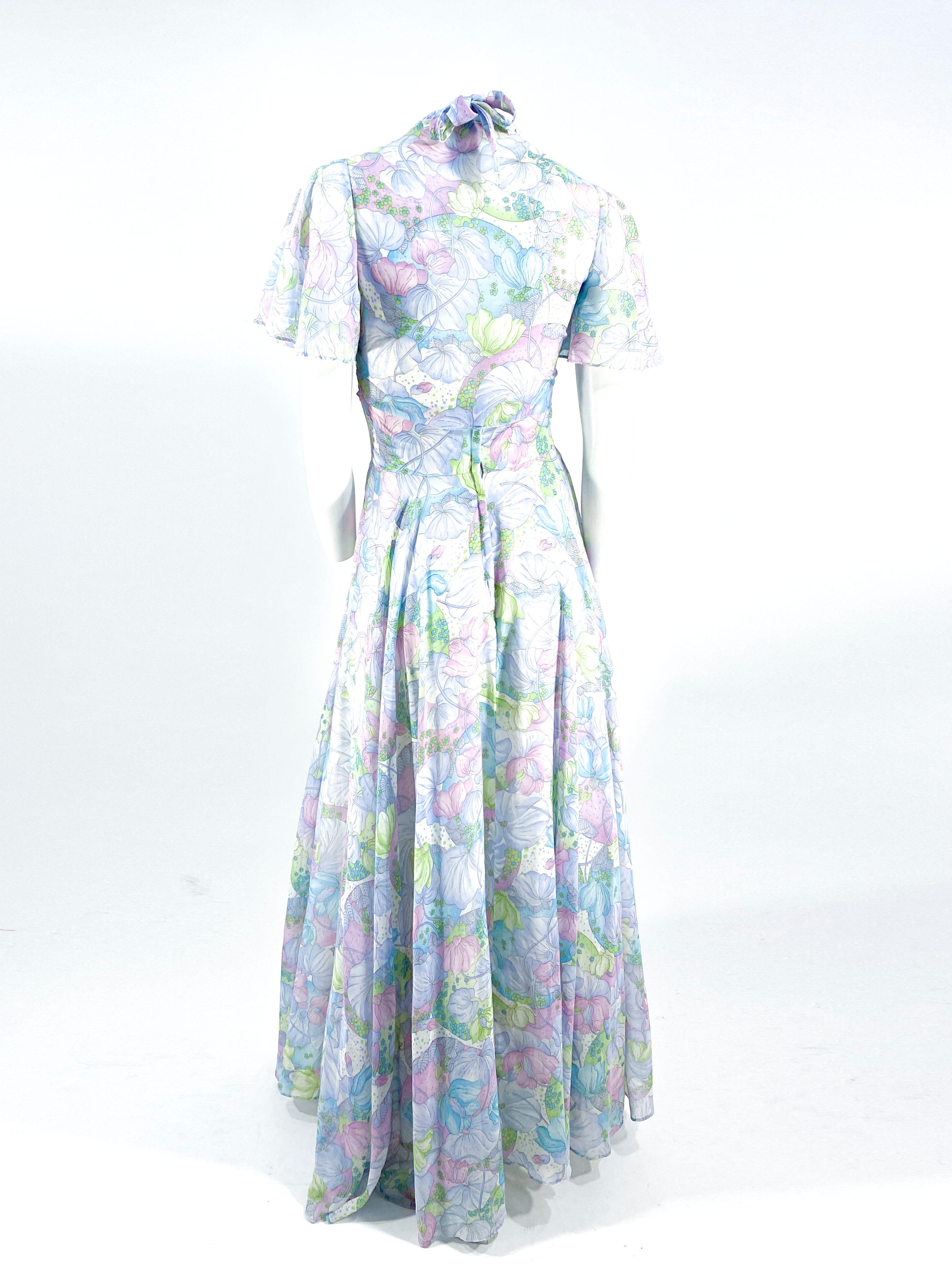 1970s pastel-colored floral printed dress featuring a halter bodice, flowing skirt, and a plunging backline. The matching bolero shrug has sheer fluted sleeves and a tie closure in the front. The back has a nylon zipper closure.