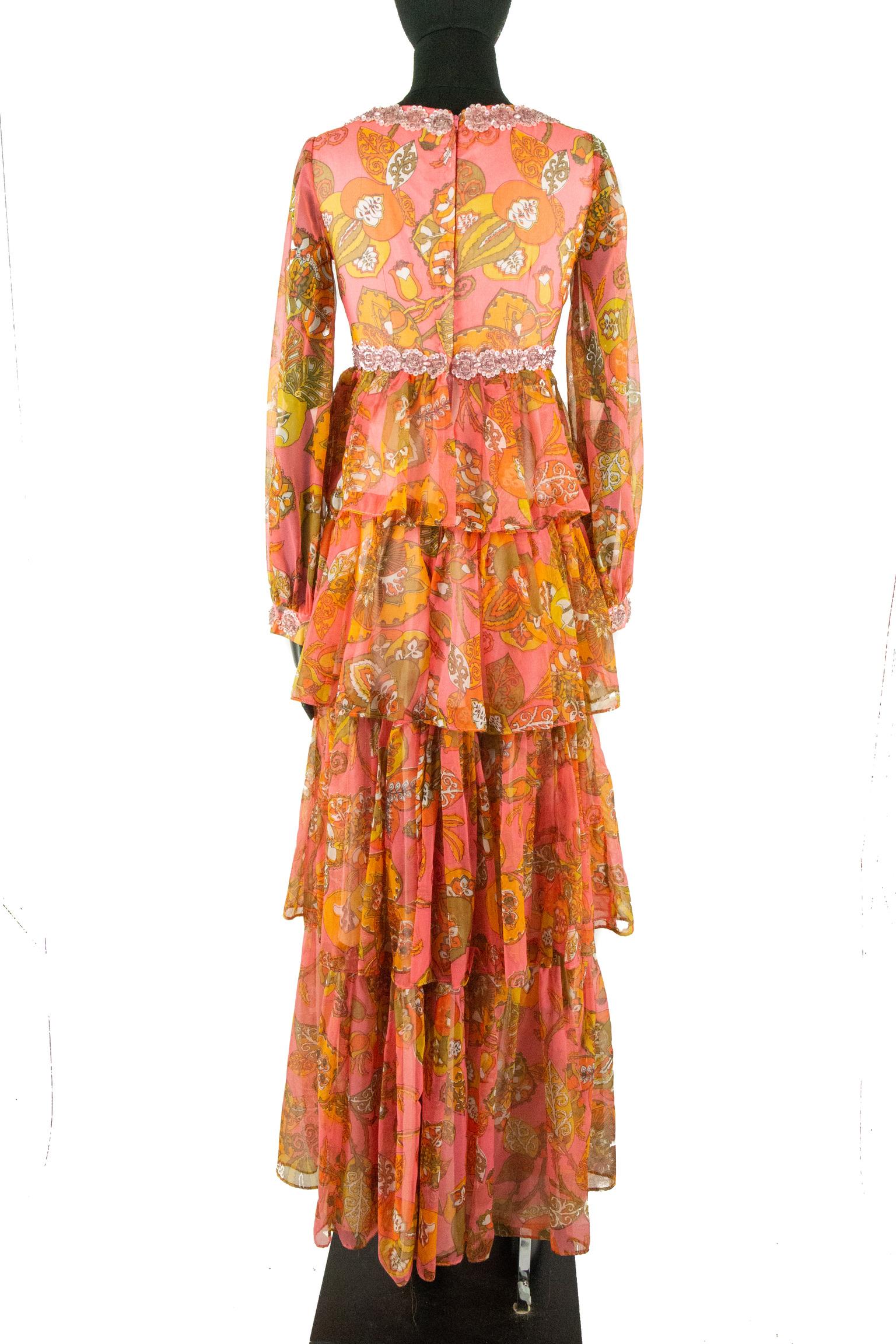 A Vintage 1970s Pauline dress; featuring a coral psychedelic print of peach and white flower swirling into golden-brown leaves. The bodice features a scooped neckline and empire waistline, both of which are embellished with small roses made of