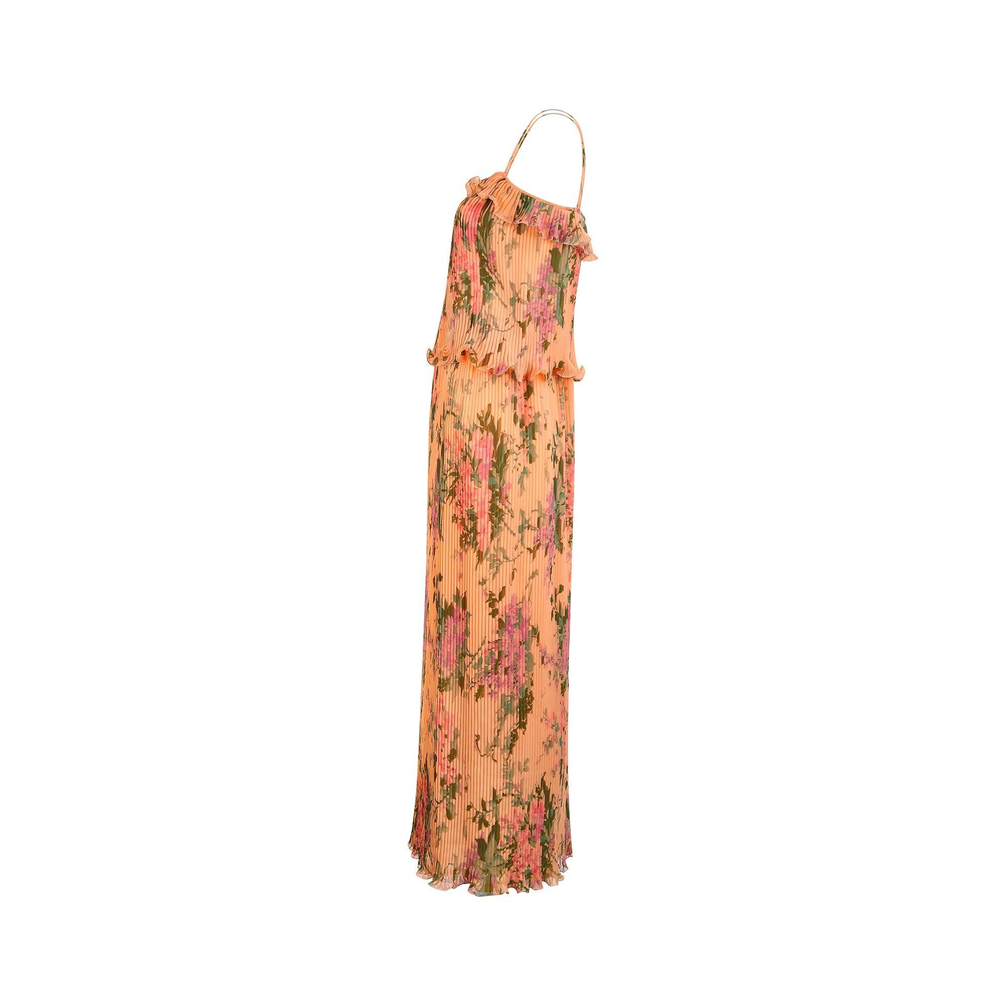This 1970s maxi dress was bought in Paris and is crafted from man-made peach chiffon splashed with bold lilac and pink florals. Pleated all over with an innovative technique that ensures the folds remain when wet or washed, it has a playful ruffle