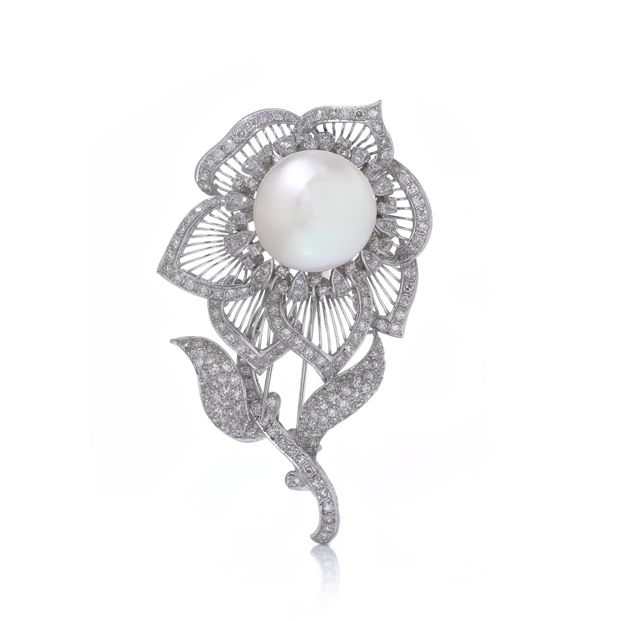 Broche florale des années 1970, sertie d'une grosse perle ronde naturelle en son centre, encadrée de pétales ajourés et de diamants pavés. Réalisée en argent et en or blanc 18 ct, cette pièce allie un design organique à un travail de diamantaire de