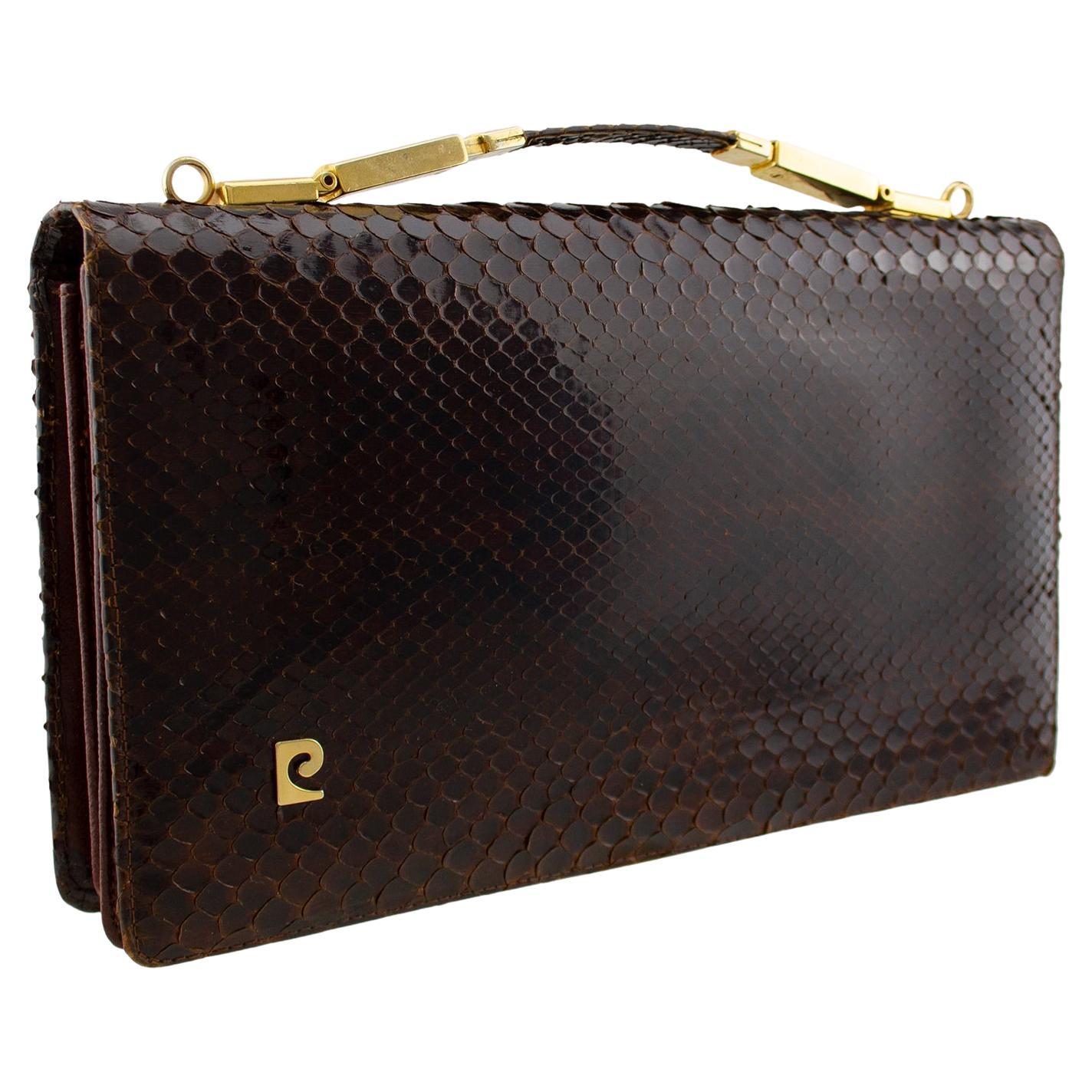 Beautiful Pierre Cardin brown skin clutch from the 1970s. Rectangular with gold tone metal hardware and retractable top handle. Small PC logo on left bottom corner. Front flap opens to a brown leather and suede interior. Accordion style with two