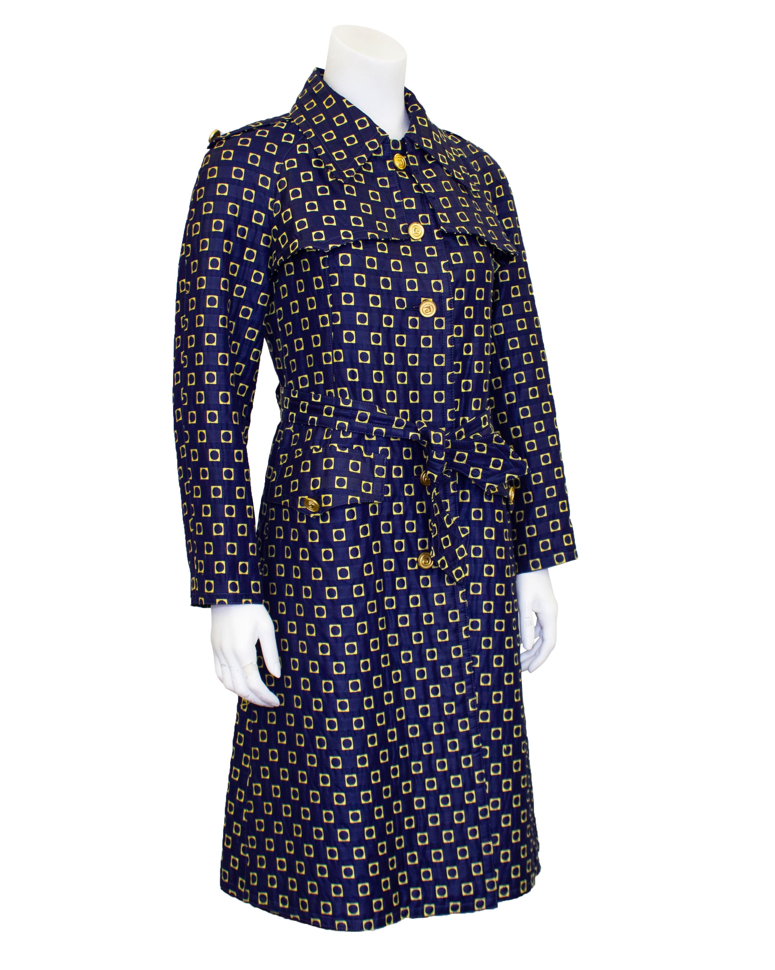 Mod 1970s Pierre Cardin trench coat. Navy blue cotton brocade with all over geometric yellow squares that have rounded interiors. Round gold tone metal buttons with the Pierre Cardin logo. Classic trench coat shape with front and back vents,