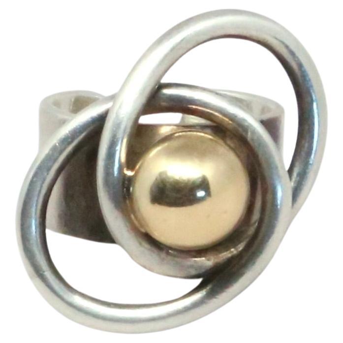 Questo anello di Pierre Cardin degli anni '60 è un ottimo esempio del suo stile audace e spaziale. È realizzato in argento sterling con una sfera in oro 14k al centro, circondata da bande d'argento Looping che le conferiscono un aspetto scultoreo,