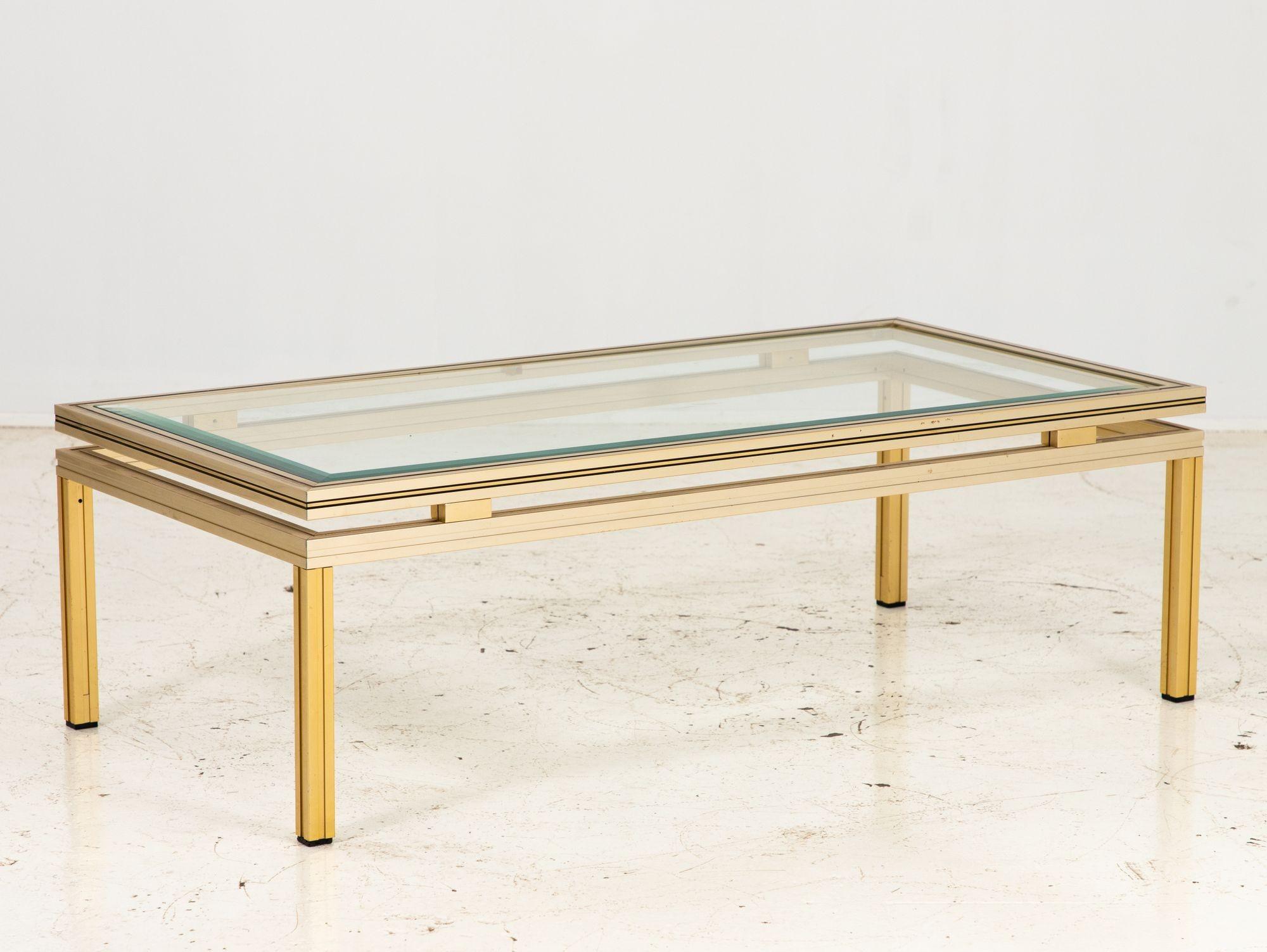 A 1970s Pierre Vandel style brass and stainless steel coffee table. A rectangular French cocktail or coffee table with four square legs and a beveled glass top. Wear consistent with age and use.