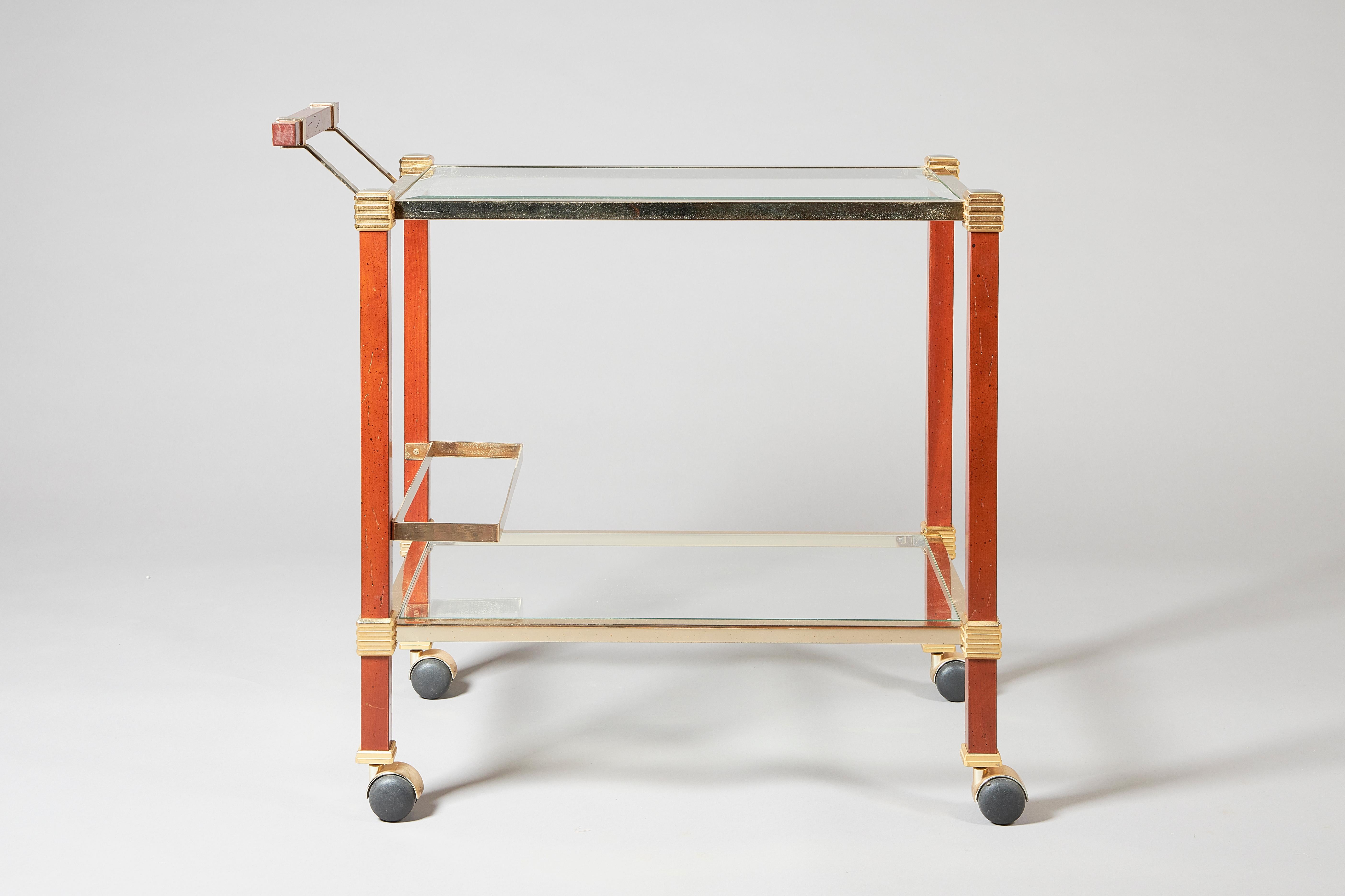 A two-tier drinks cart, attributed to Pierre Vandel, France, circa 1970, with removable glass inserts, gilt and silvered metal mounts and block fruitwood supports, on black castors.