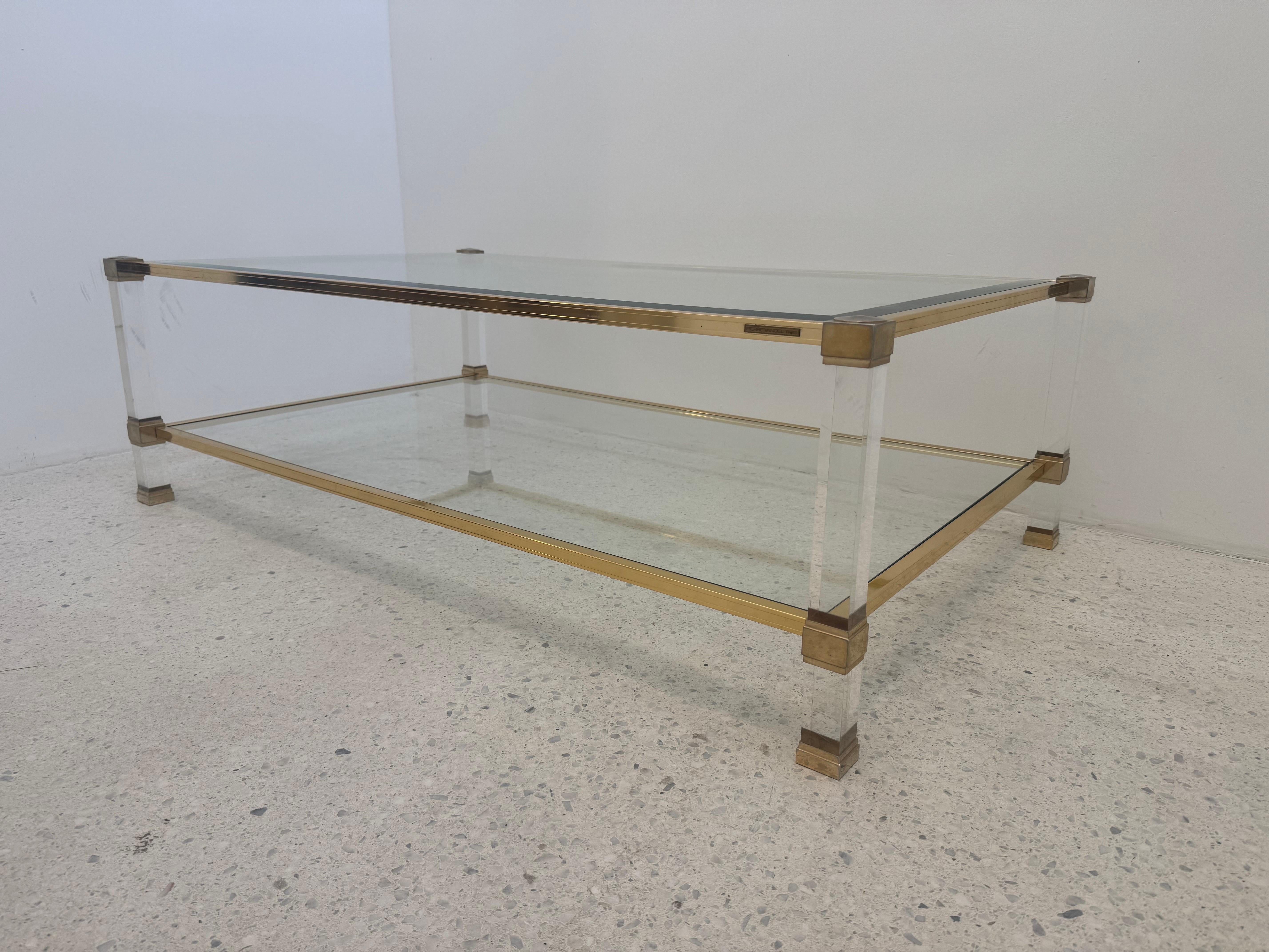 Questo raffinato tavolino da caffè degli anni '70 di Pierre Vandel esemplifica il caratteristico mix di modernismo francese e stile Hollywood Regency del designer. La struttura è caratterizzata da gambe in lucite trasparente unite da un'intelaiatura