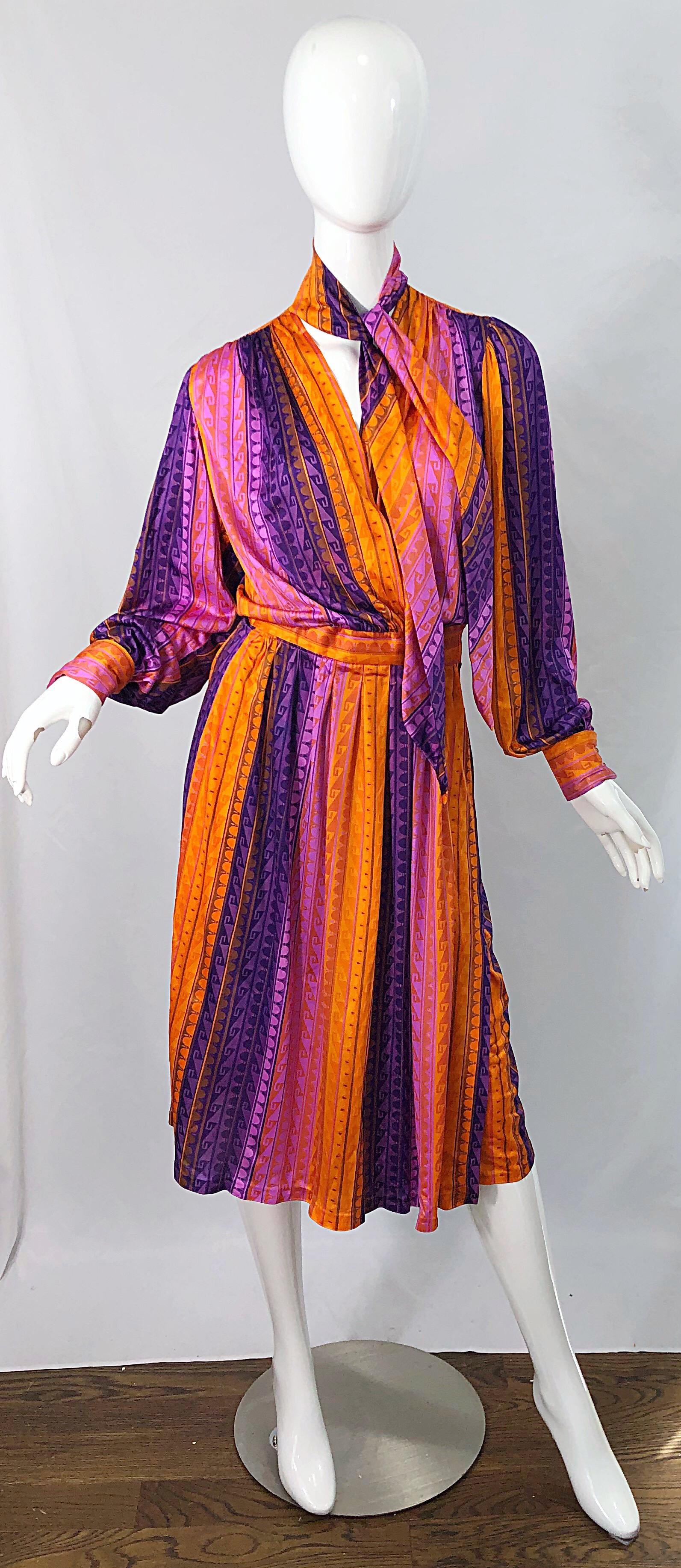 Pretty 1970s orange, pink and purple slinky jersey wrap dress with attached neck scarf ! Features vibrant colors with an Aztec like print throughout. Colorful rhinestone buttons at each French cuff. Wrap style that has interior adjustable velcro