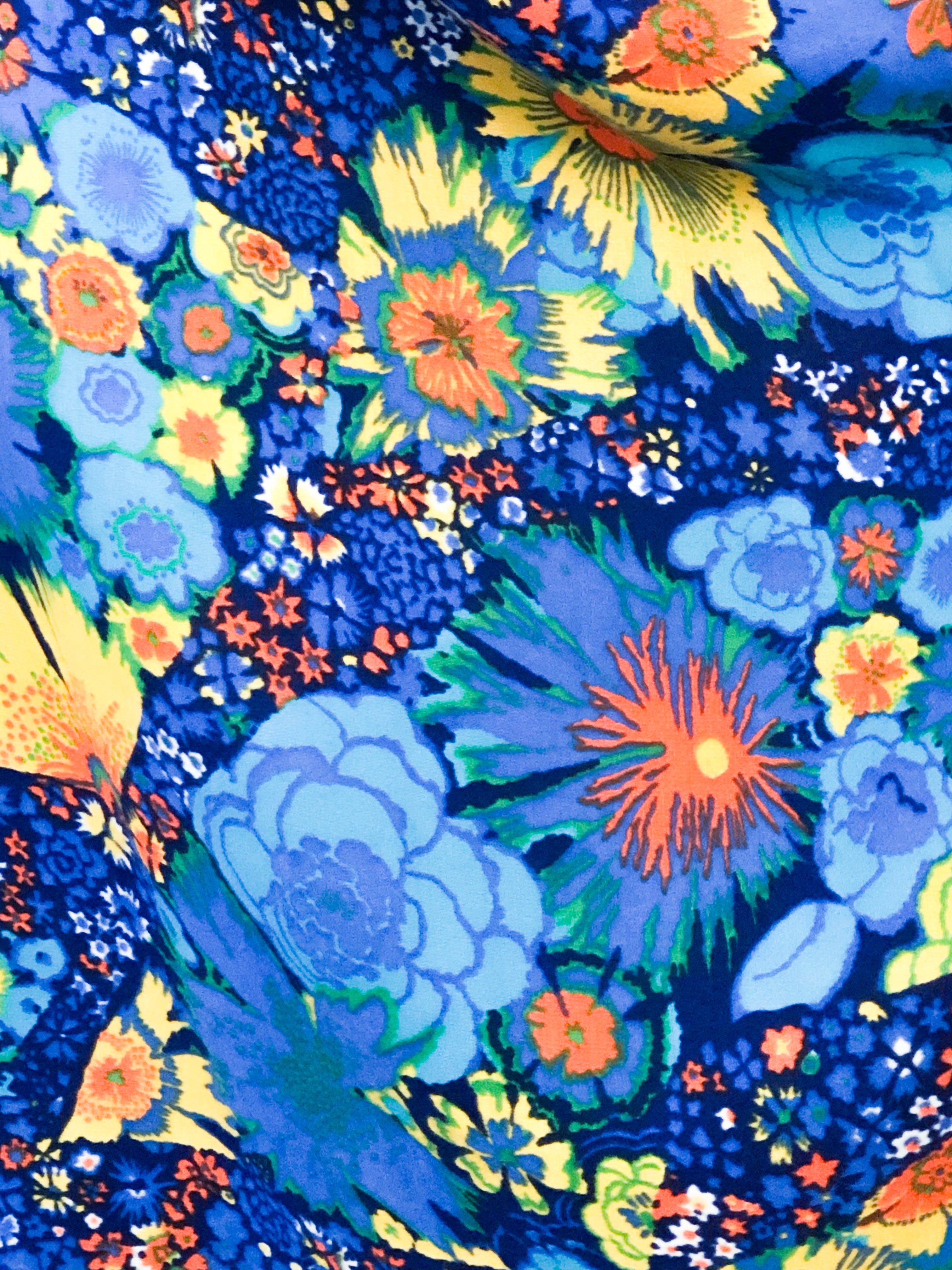 1970's Psychedelic floral printed jumpsuit featuring neon blues, yellows, and oranges. The halter top is secured behind the neck with a tie to complement the plunge back line and the empire waist at the face of the suit. The pants of this suit are