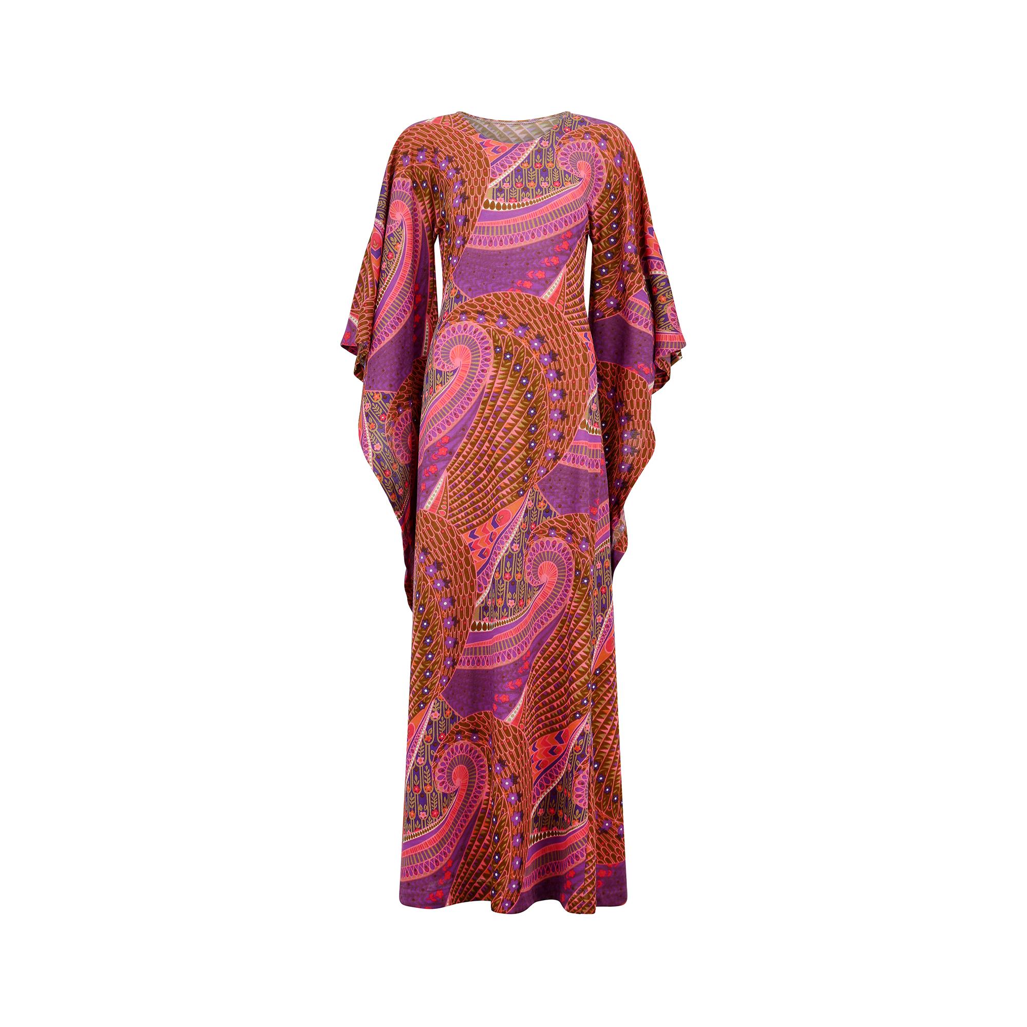 Fabulous 1970s angel sleeve psychedelic print dress cut in a classic elongated sheath shape with long flowing skirt and rounded neckline. It features a striking print in a distinctive paisley design, with floral details and in shades of purple, deep