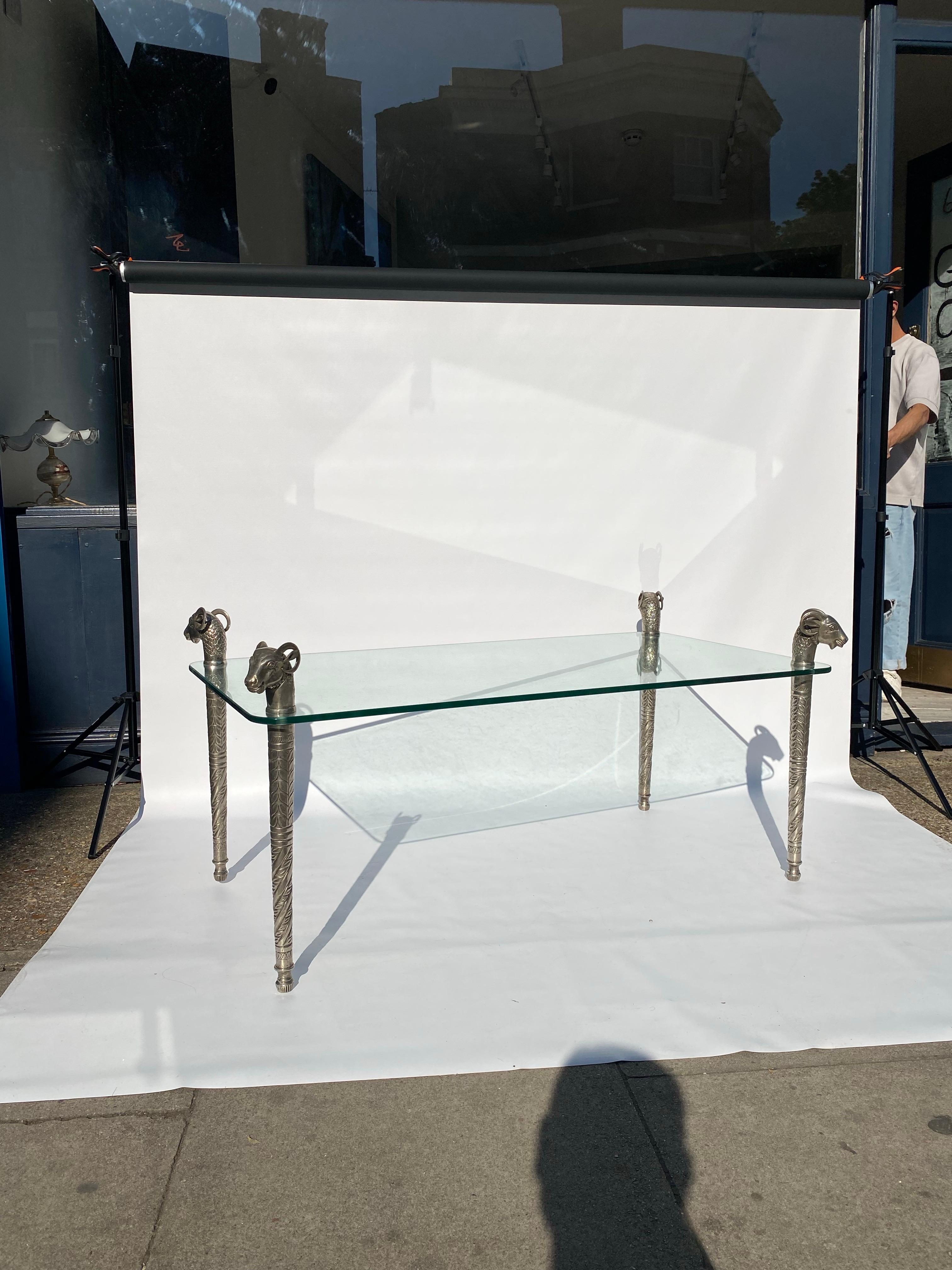 Il s'agit d'une table étonnante comportant quatre pieds en métal argenté avec des têtes de béliers. 
Les pieds suivent un dessin complexe de débosselage incurvé. La partie proche du sommet se dévisse et le plateau en verre est inséré. Des détails
