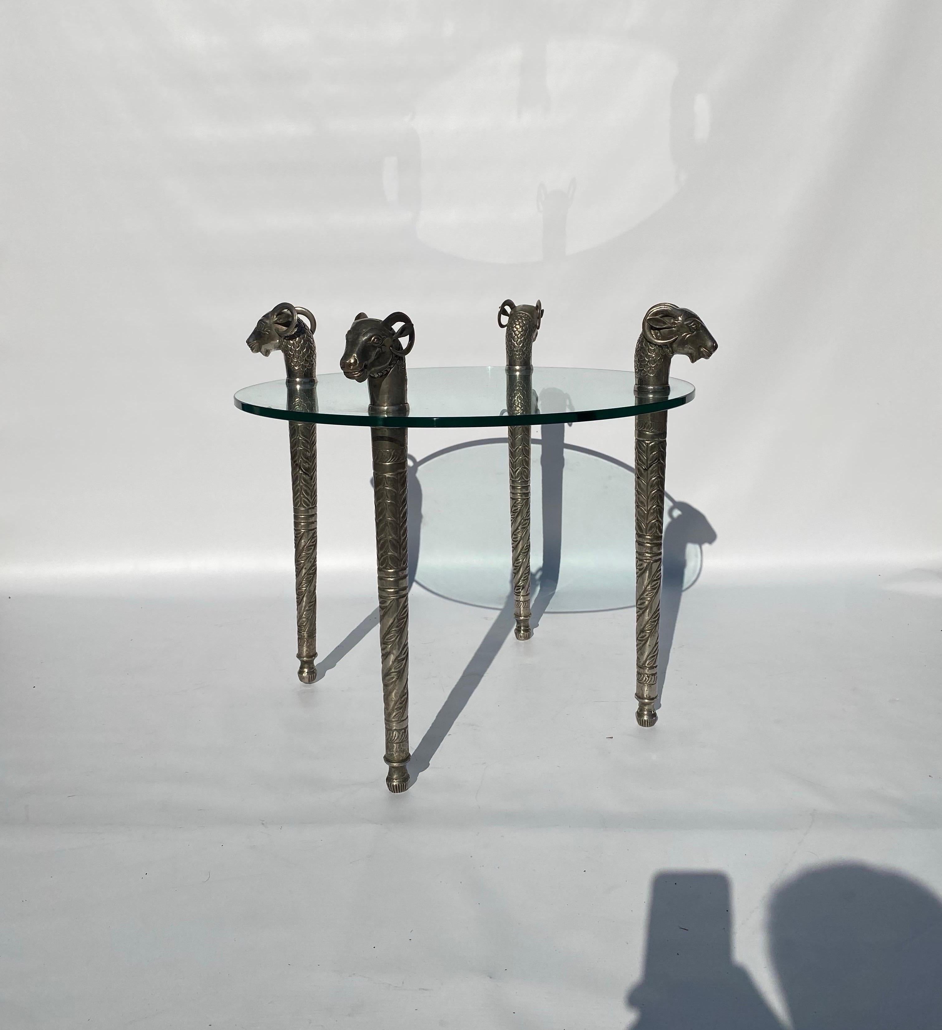 Il s'agit d'une table étonnante comportant quatre pieds en métal argenté avec des têtes de béliers. 
Les pieds suivent un dessin complexe de débosselage incurvé. La partie proche du sommet se dévisse et le plateau en verre est inséré. Les détails