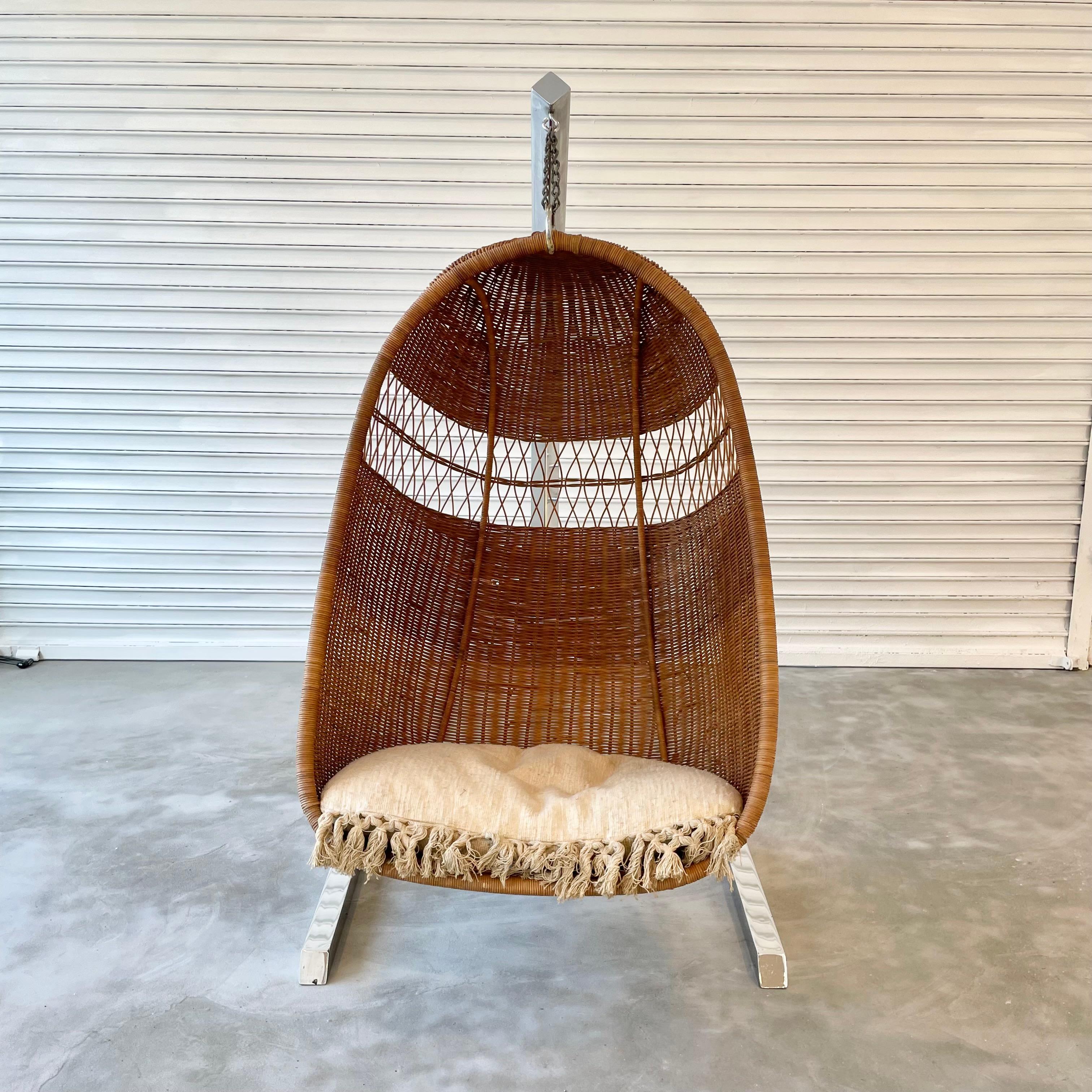 Rare sculptural rattan and wicker hanging chair. Hanging from an angular chrome stand. Stunning design. Great scale. Multiple window cut-outs to see through chair. Perfect indoors or outside in a covered deck. Suspended by heavy duty chain.