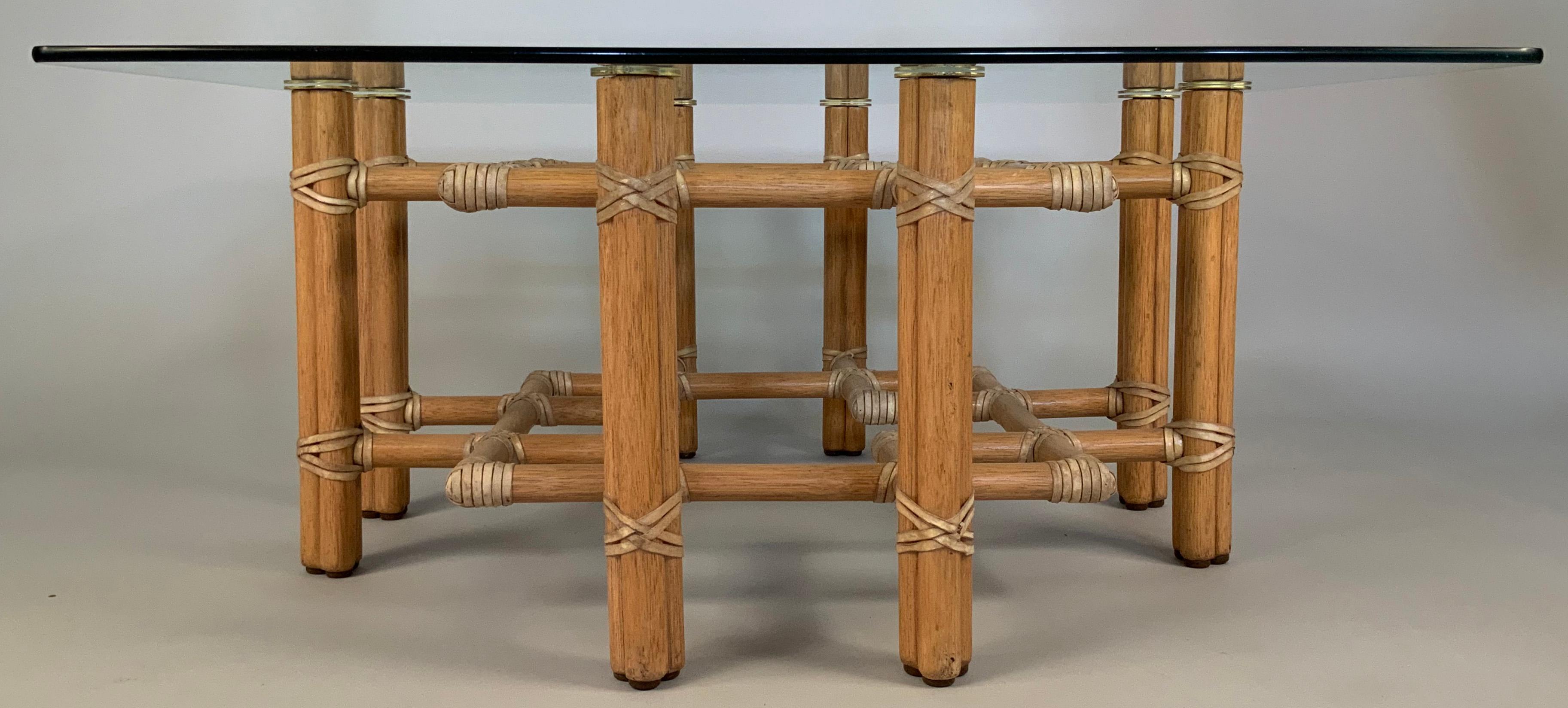 A beautiful vintage 1970s coffee table by McGuire of San Francisco, with a base of rattan and bamboo, with leather lacing, in an intricate double square design, supporting a square glass top. The tops of the base are finished with eight solid brass
