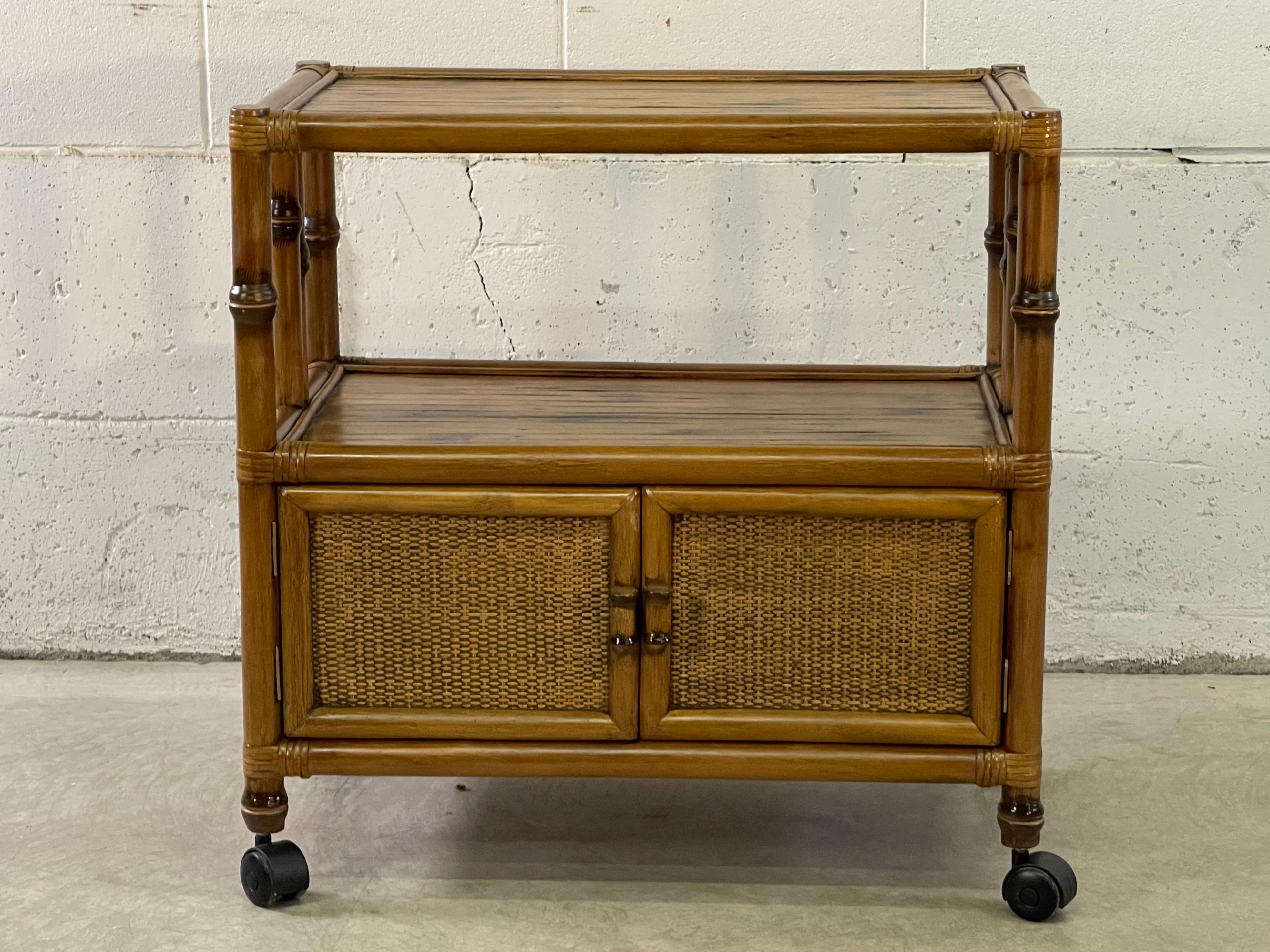 Vintage 1970s rattan rolling serving cart with additional storage. The cart has two shelves and additional space to store on the bottom. The rattan has burnt accents all over the cart.
