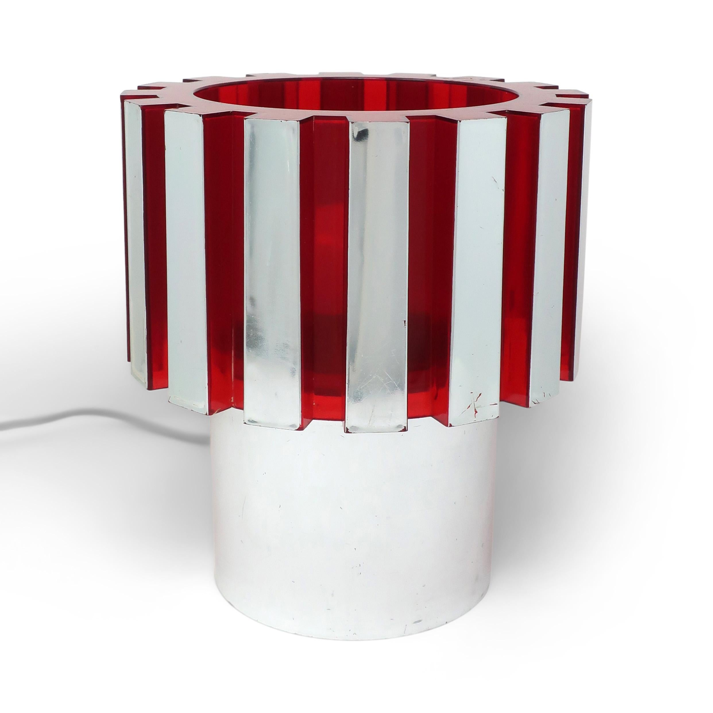 A very cool red and chrome colored plastic desk lamp by C.N. Burman.  Cast in a single form with a cylindrical base and notched gear link top.  The alternating chrome painted and transparent red sections allow the light to shine out in a fantastic