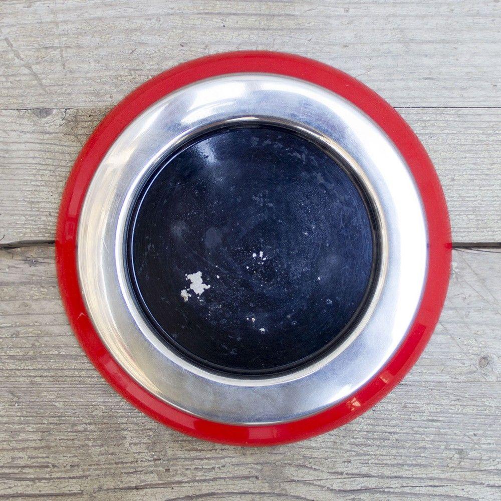 A cherry red ABS plastic base, featuring a chrome metal rim around a black enamel plate. This 1970s ashtray was designed by Sergio Asti for the furniture and decorative manufacture Kartell.