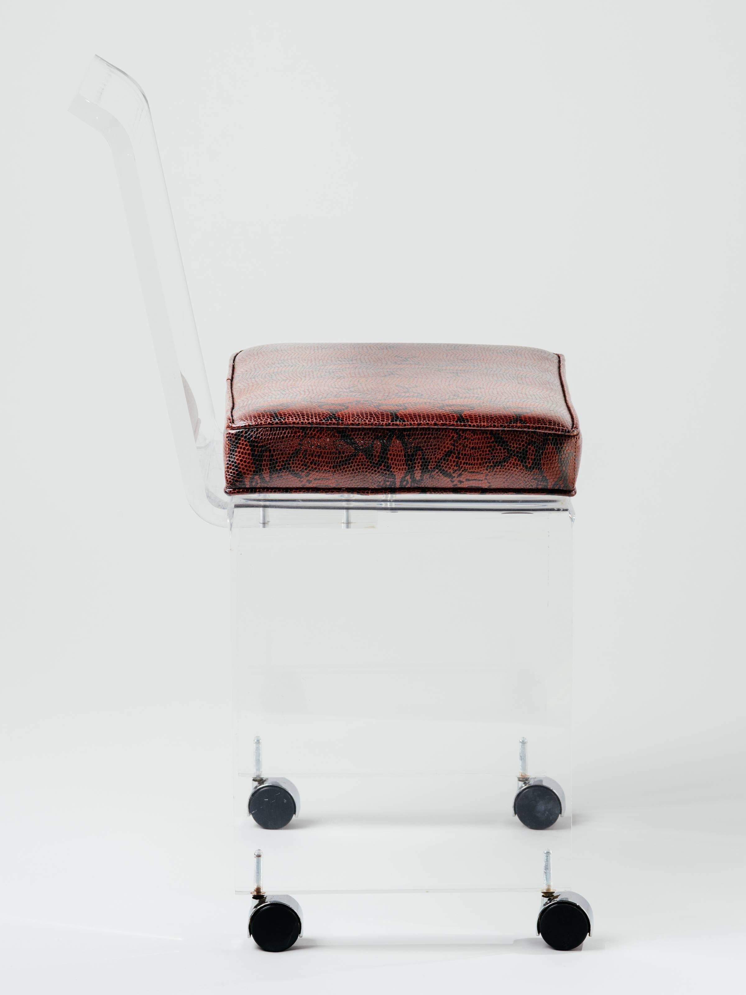 Mid-Century Modern Lucite vanity chair in genuine leather with embossed snakeskin print in deep red. It is real leather, faux python print. Stool has sleek lines with full back design, and polished bevelled edges. Features swivel casters for