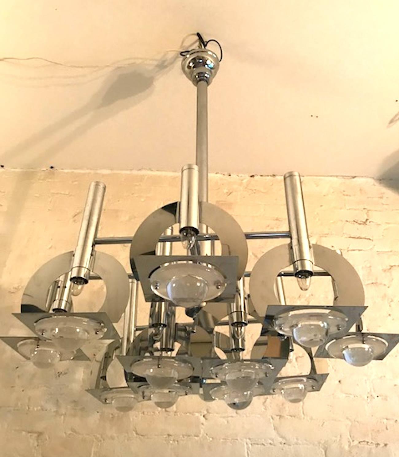 A wonderful 1970s geometric and abstract chrome and glass chandelier attributed to the Italian lighting company Reggiani. Twelve-light. Below each light is a suspended square plate with glass lens inset into it. The lens has a dome center and